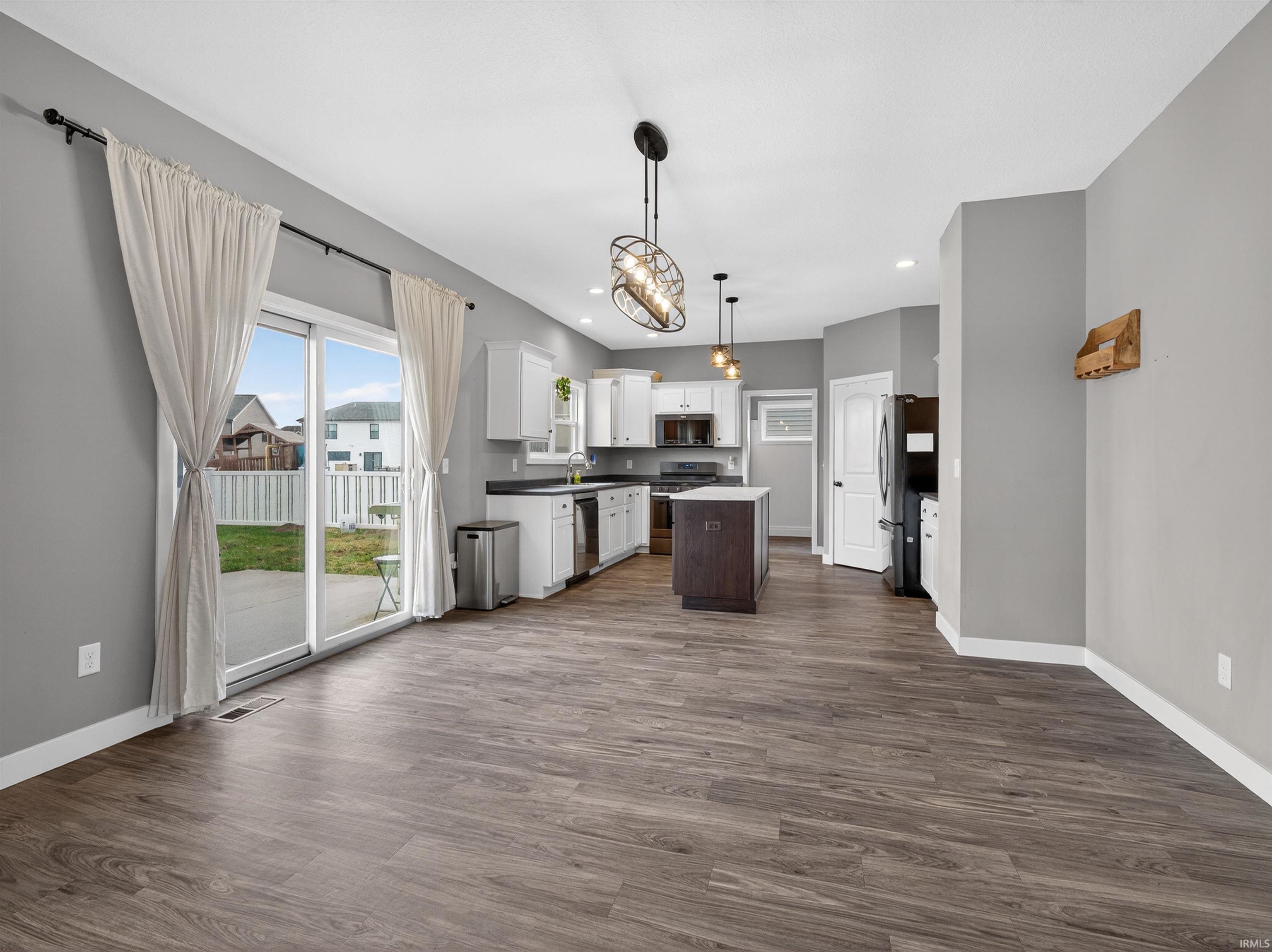 Kitchen with a center island, stainless steel appliances, open floor plan, dark countertops, and dark wood-style flooring