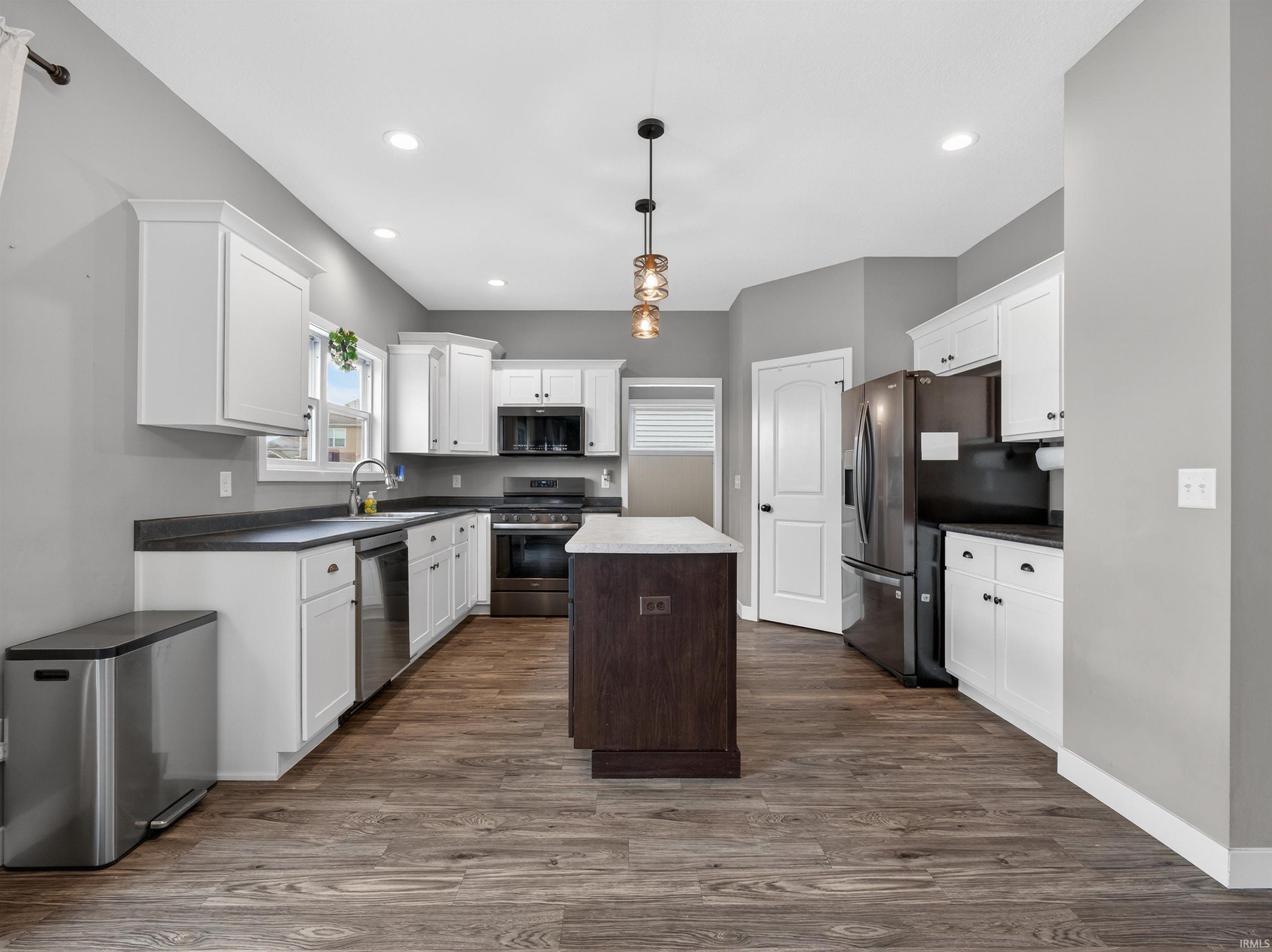 Dual tone kitchen featuring dark countertops, stainless steel appliances, two tone cabinets, dark wood-style floors, and a kitchen island