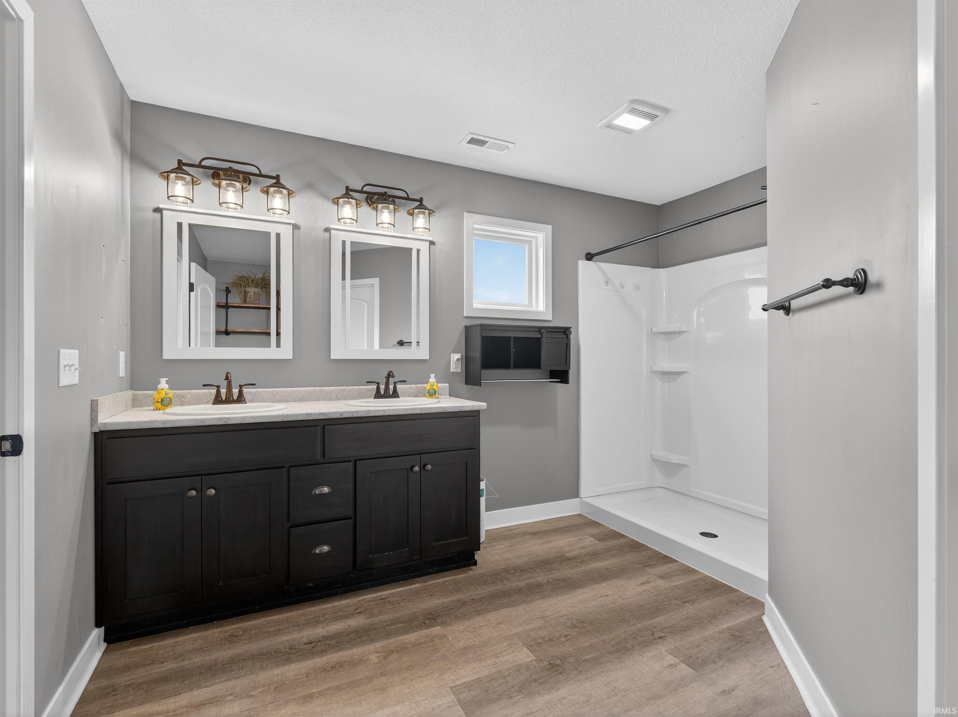 Full bathroom with double vanity, a stall shower, and light wood-type flooring