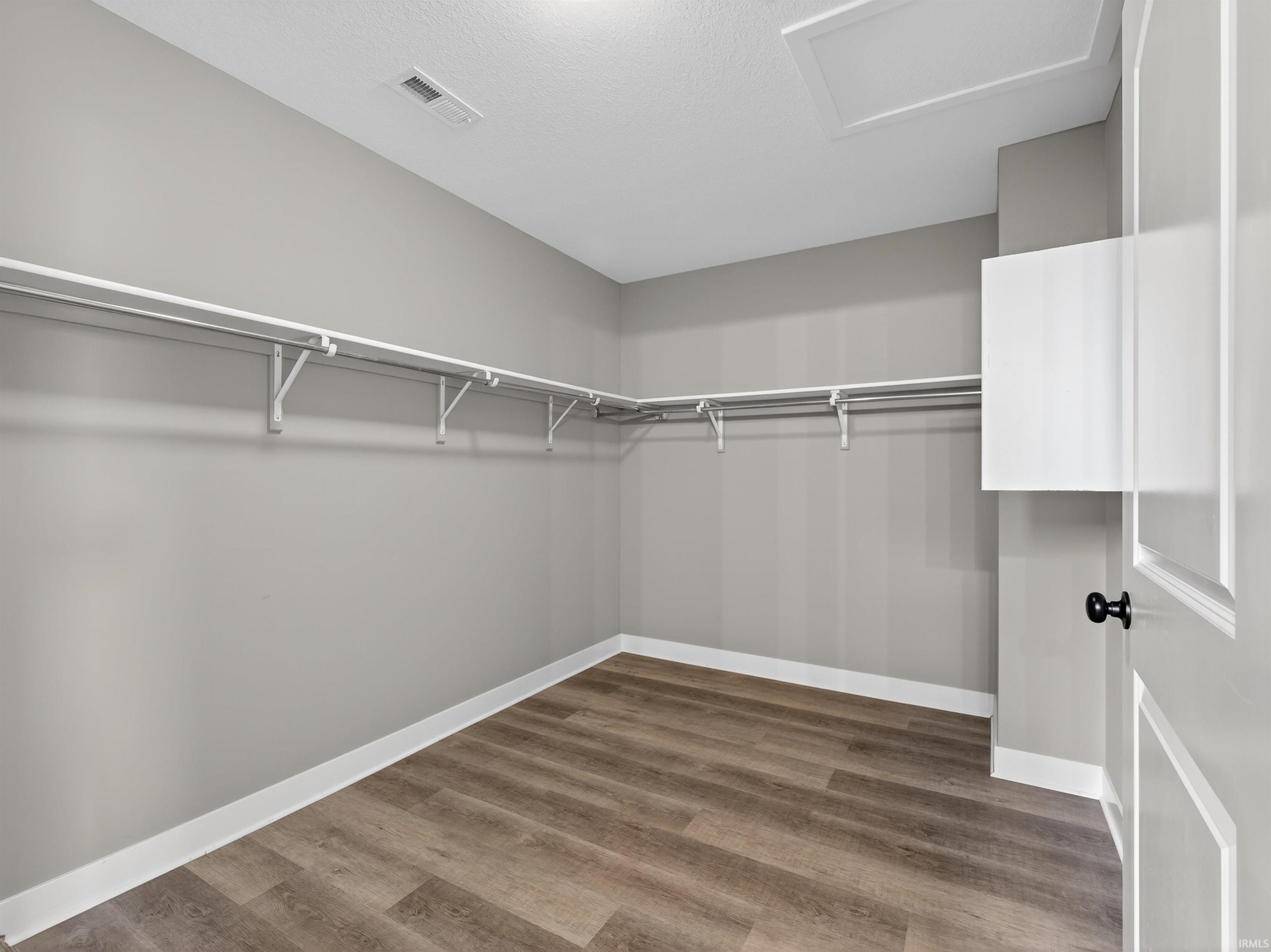 Walk in closet featuring attic access and dark wood-type flooring