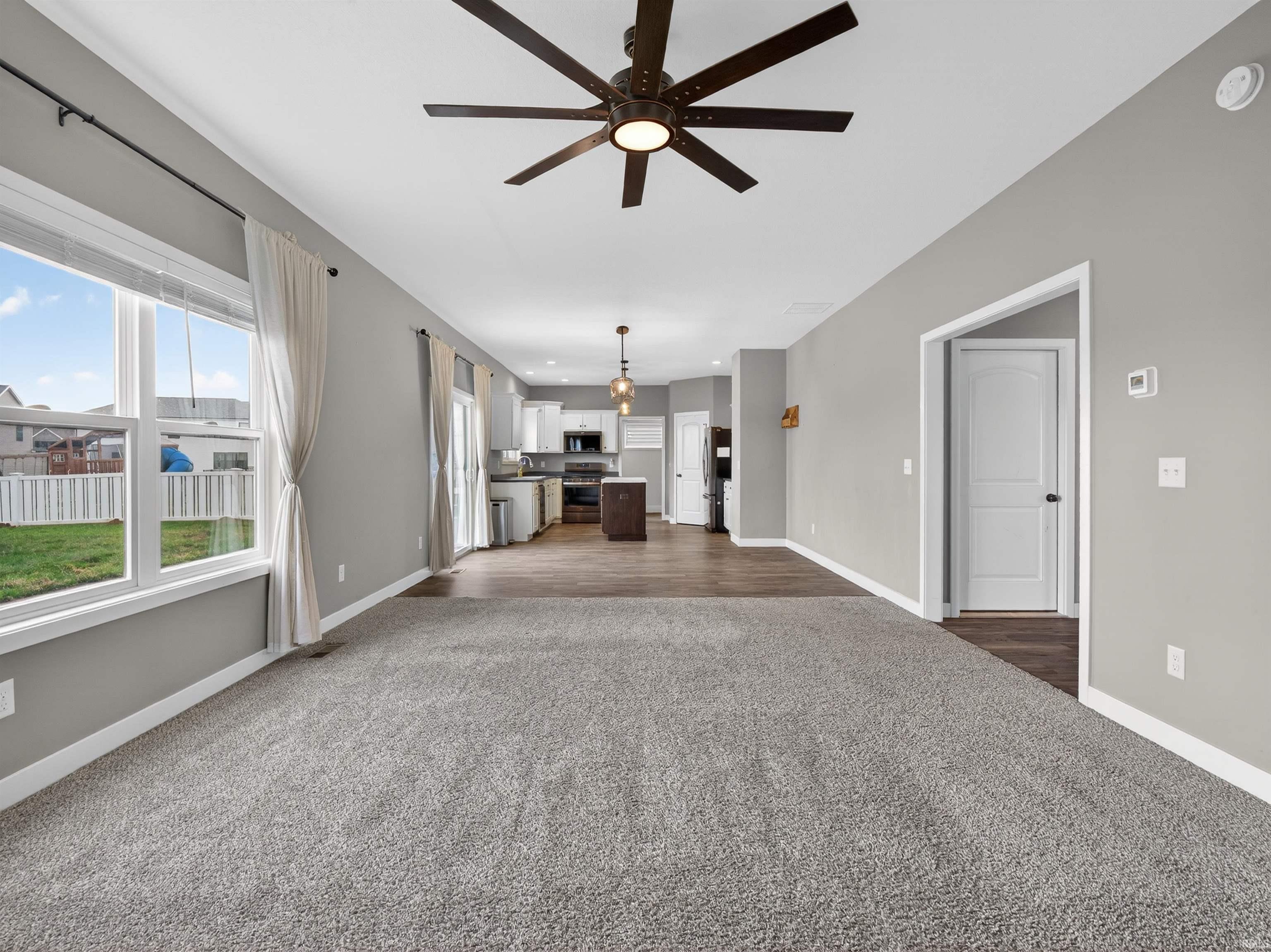 Unfurnished living room featuring ceiling fan and dark carpet