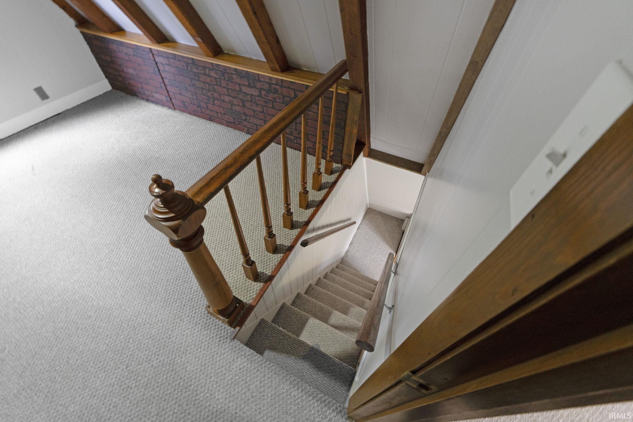 Stairway with carpet floors, brick wall, and beamed ceiling