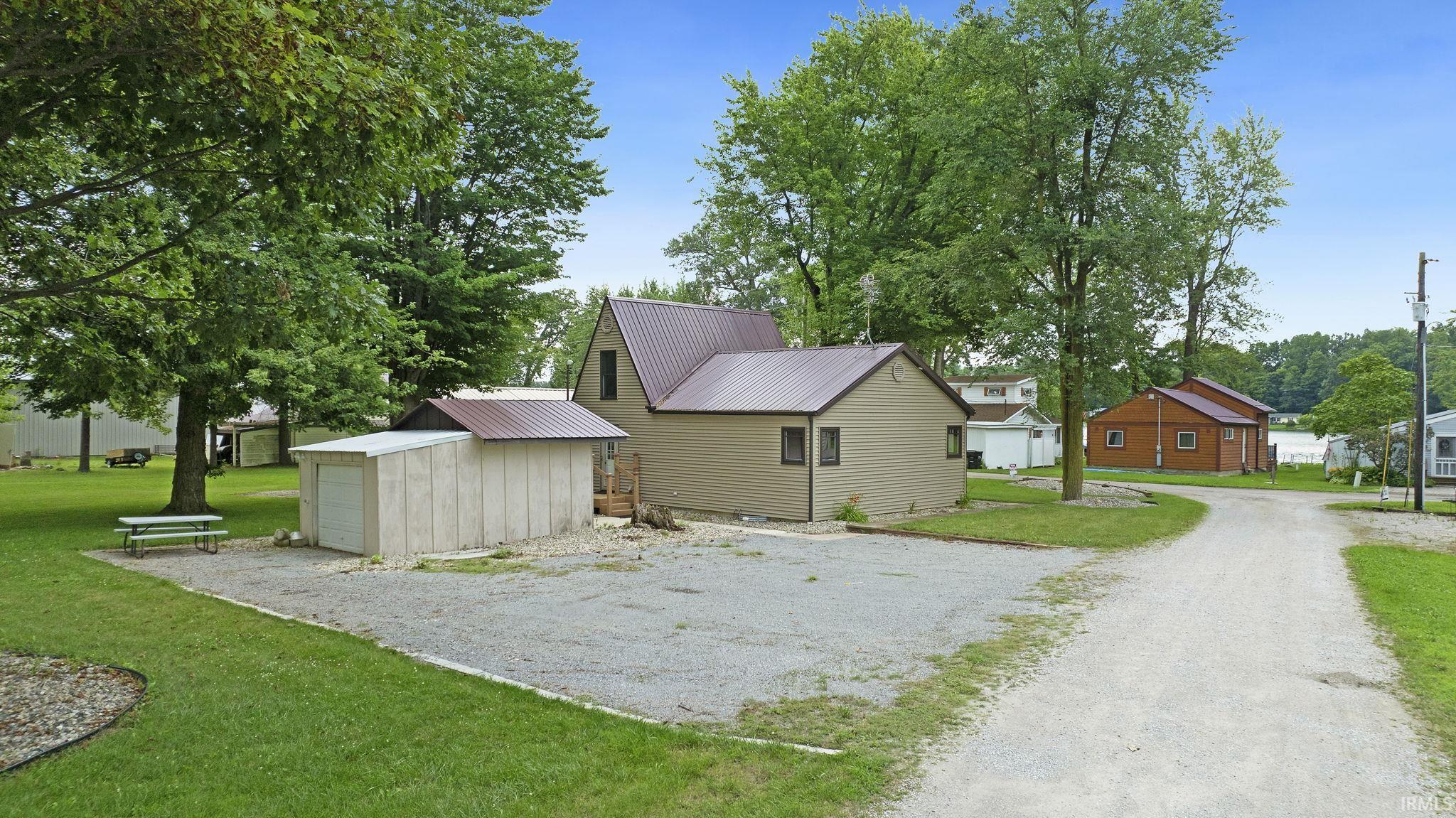 View of property exterior with a yard, a metal roof, a detached garage, driveway, and an outdoor structure