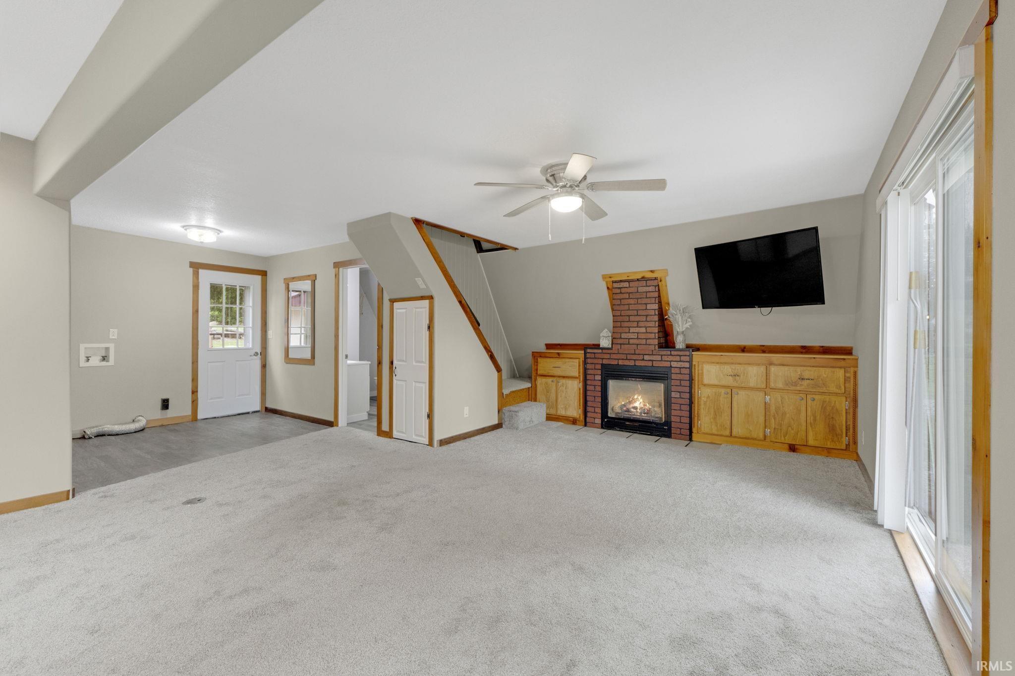 Unfurnished living room featuring plenty of natural light, light carpet, ceiling fan, and a fireplace
