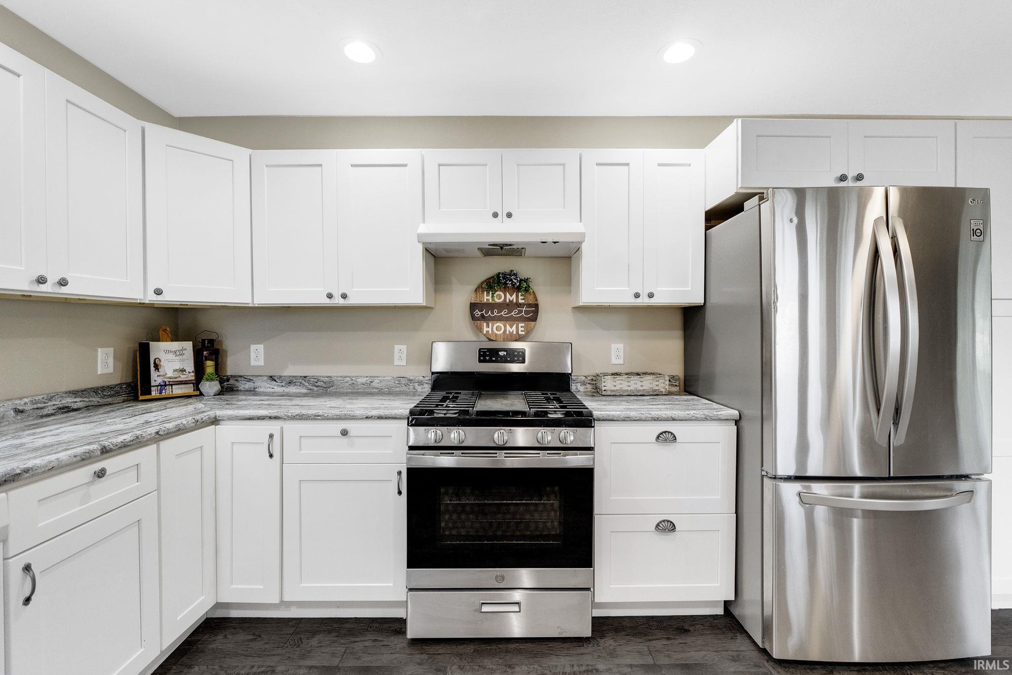 Kitchen featuring stainless steel appliances, white cabinetry, light stone countertops, recessed lighting, and dark wood-style floors