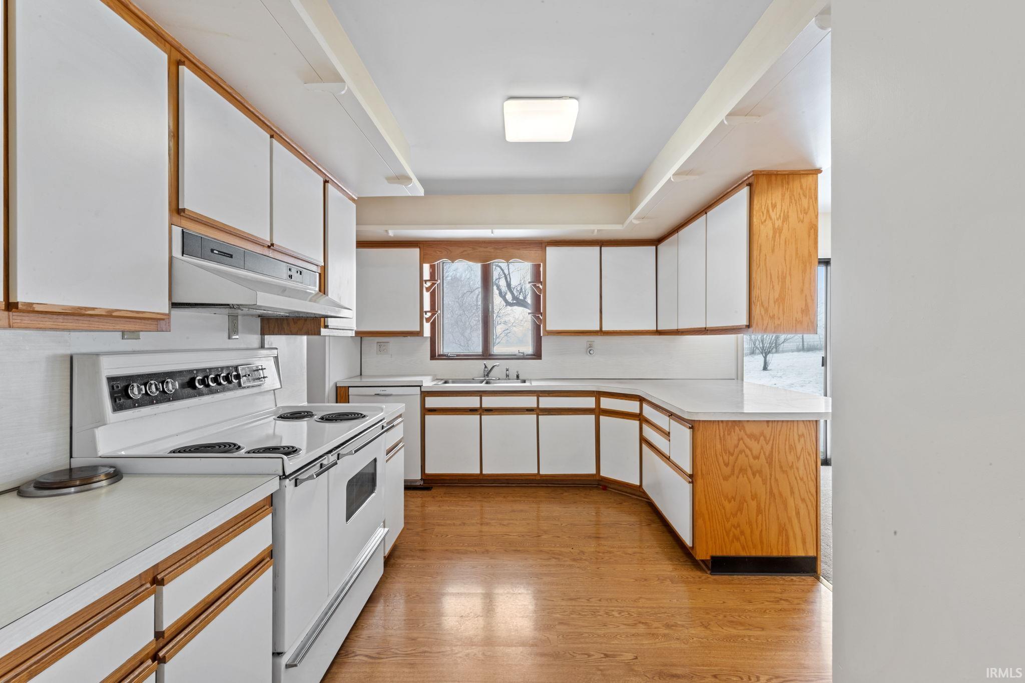 Dual tone kitchen with dual tone cabinets, white appliances, light countertops, and light wood-style floors