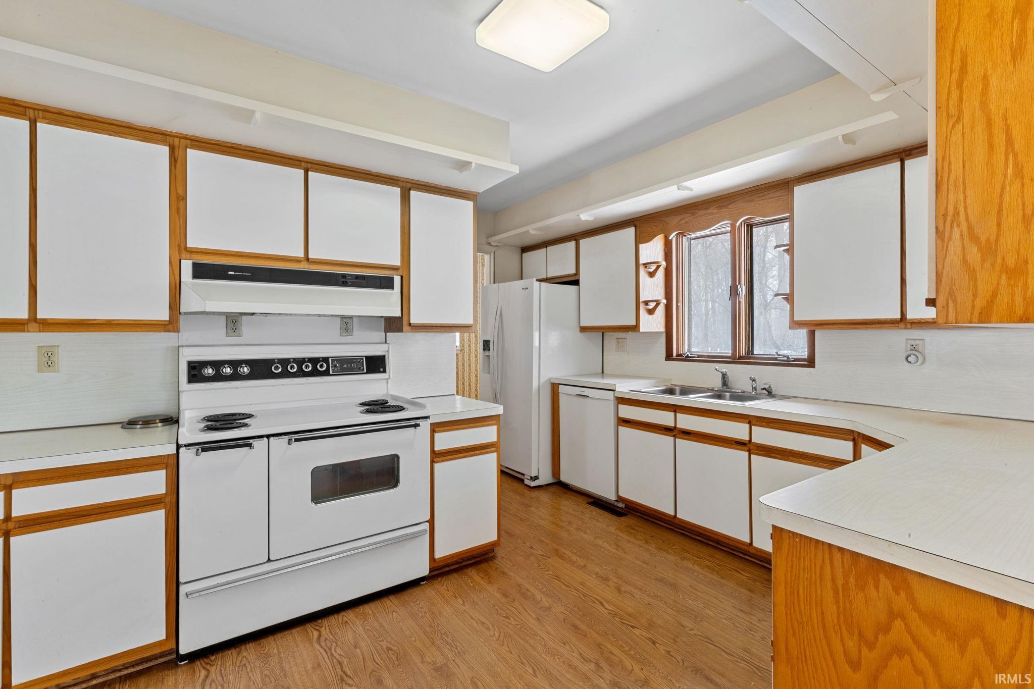 Kitchen featuring two tone cabinetry, white appliances, light countertops, and light wood-style floors