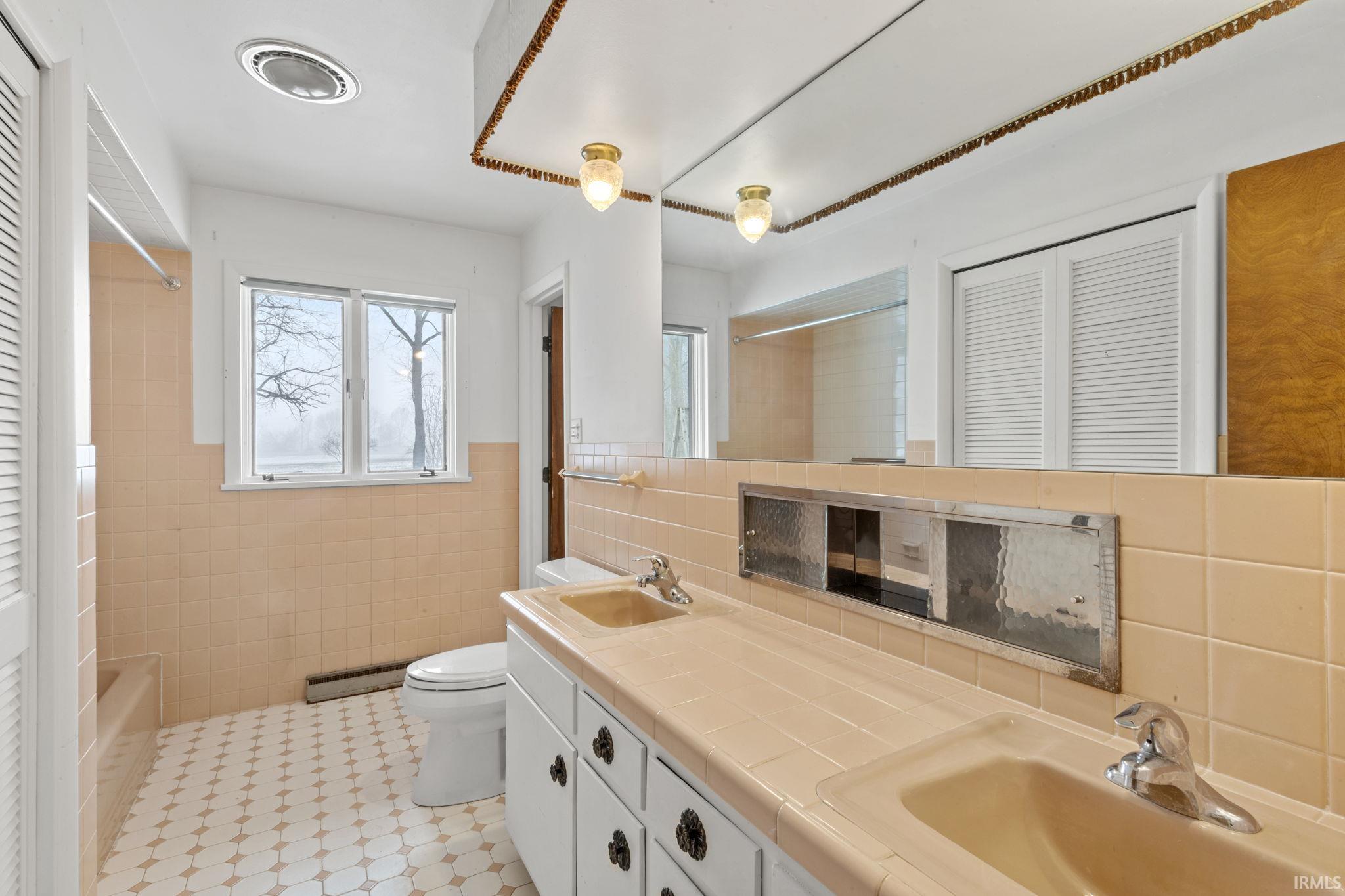 Bathroom featuring a closet, tile walls, double vanity, a baseboard radiator, and tub / shower combination