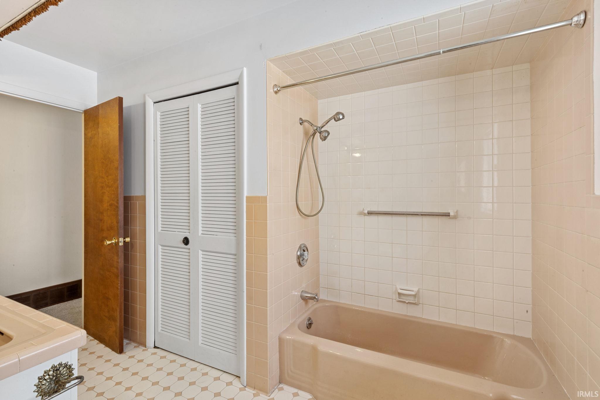 Full bath featuring a closet, bathtub / shower combination, light flooring, and tile walls