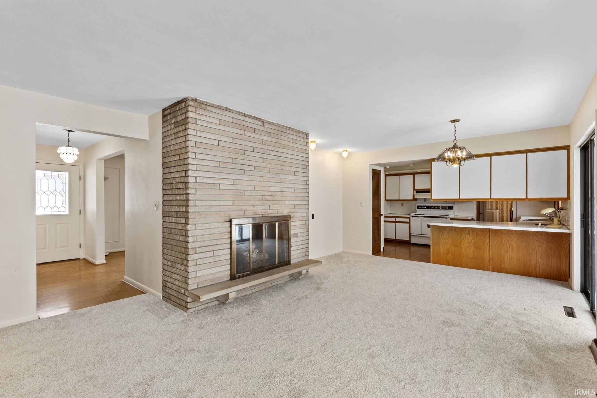 Unfurnished living room with suspended lighting, dark carpet, and a fireplace