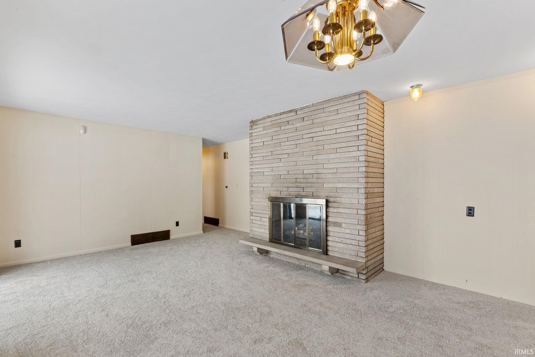 Unfurnished living room featuring carpet floors, a fireplace, and a chandelier