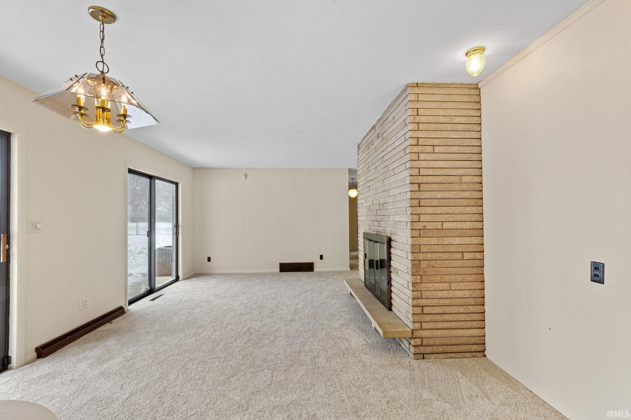 Unfurnished living room featuring a brick fireplace, light carpet, and a chandelier