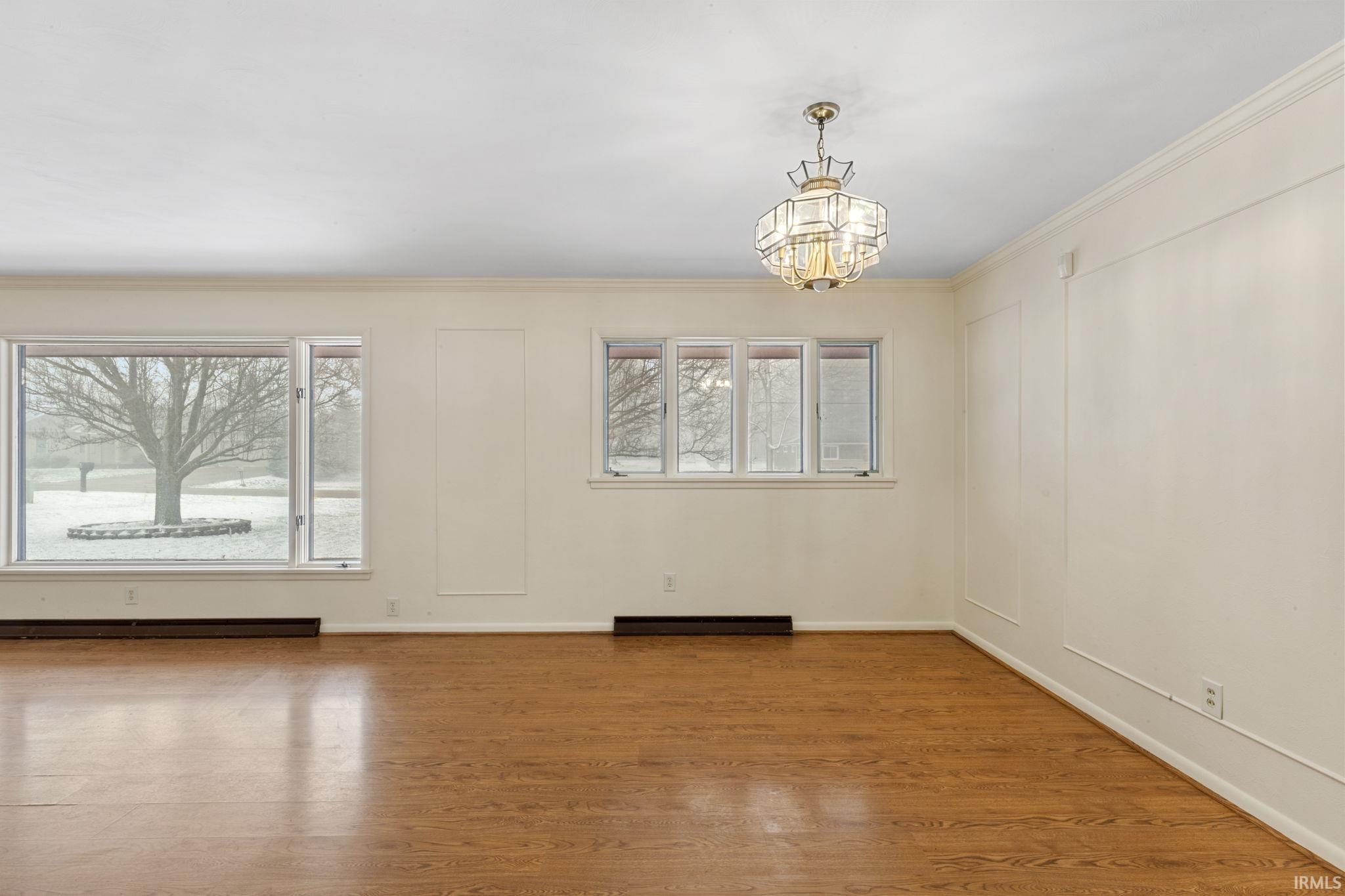 Empty room featuring ornamental molding, wood finished floors, a decorative wall, a chandelier, and baseboard heating