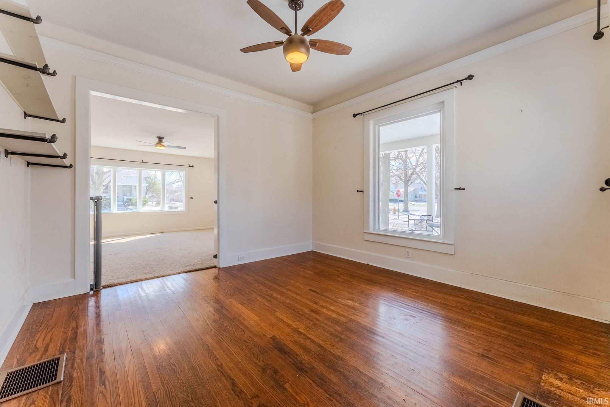 Empty room featuring dark wood-type flooring, ceiling fan, and crown molding