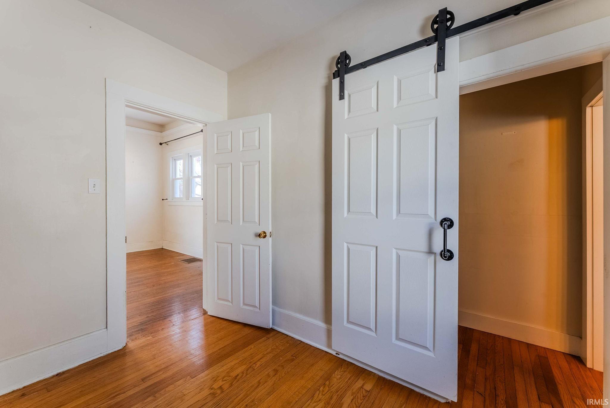 Unfurnished bedroom with a barn door and light wood finished floors