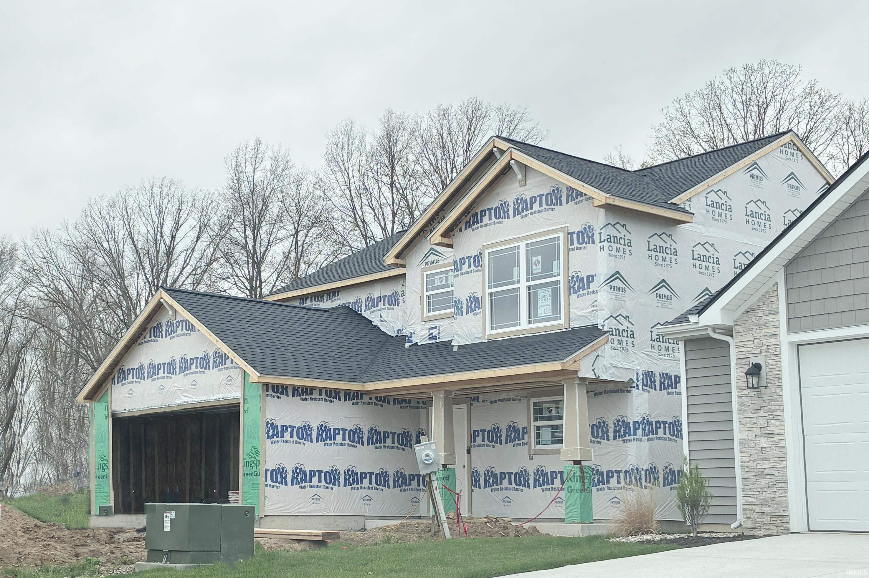 New construction residential property featuring a dark shingle roof, wrapped exterior ready for finishing, and visible window installation