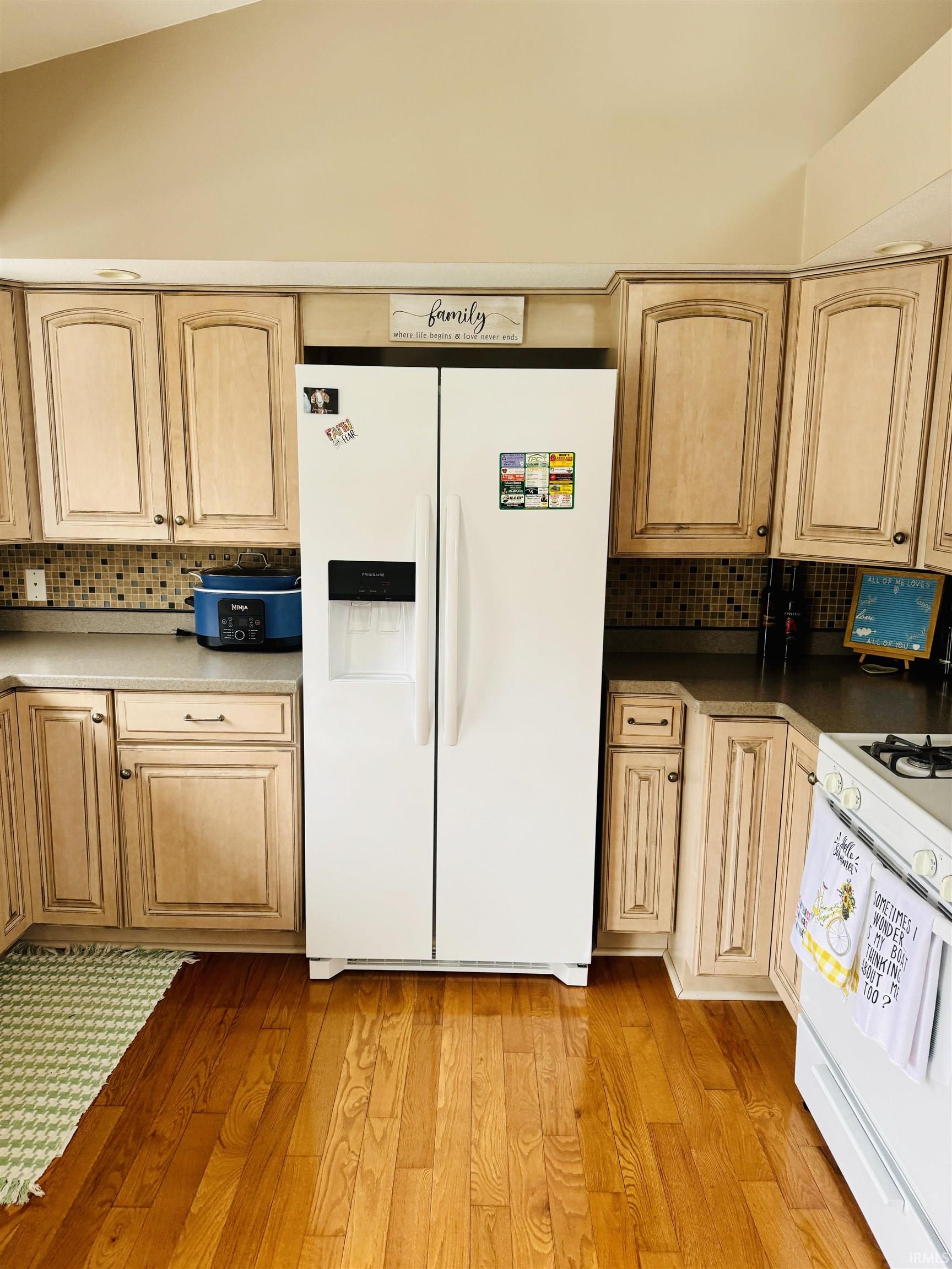 Kitchen featuring decorative backsplash, white appliances, light wood finish cabinetry, and light wood-type flooring