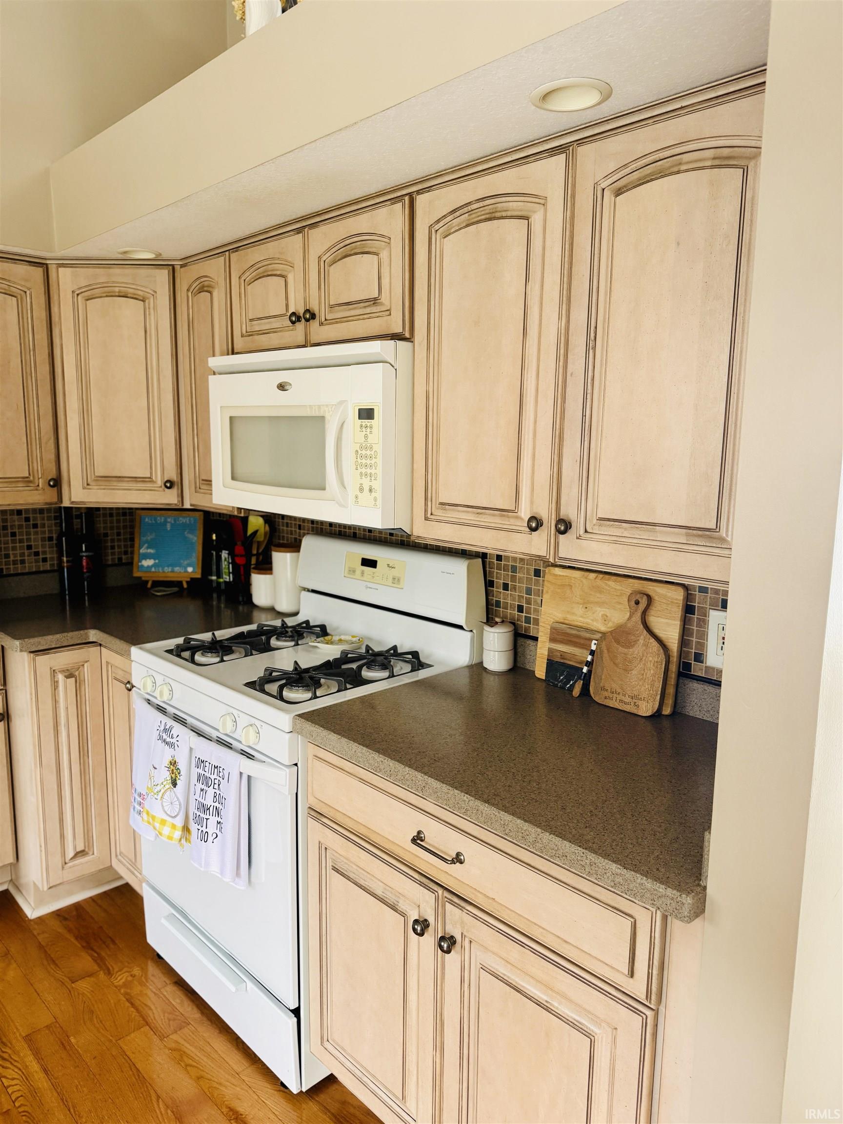Kitchen featuring white appliances, light wood finish cabinets, backsplash, dark countertops, and light wood-style floors