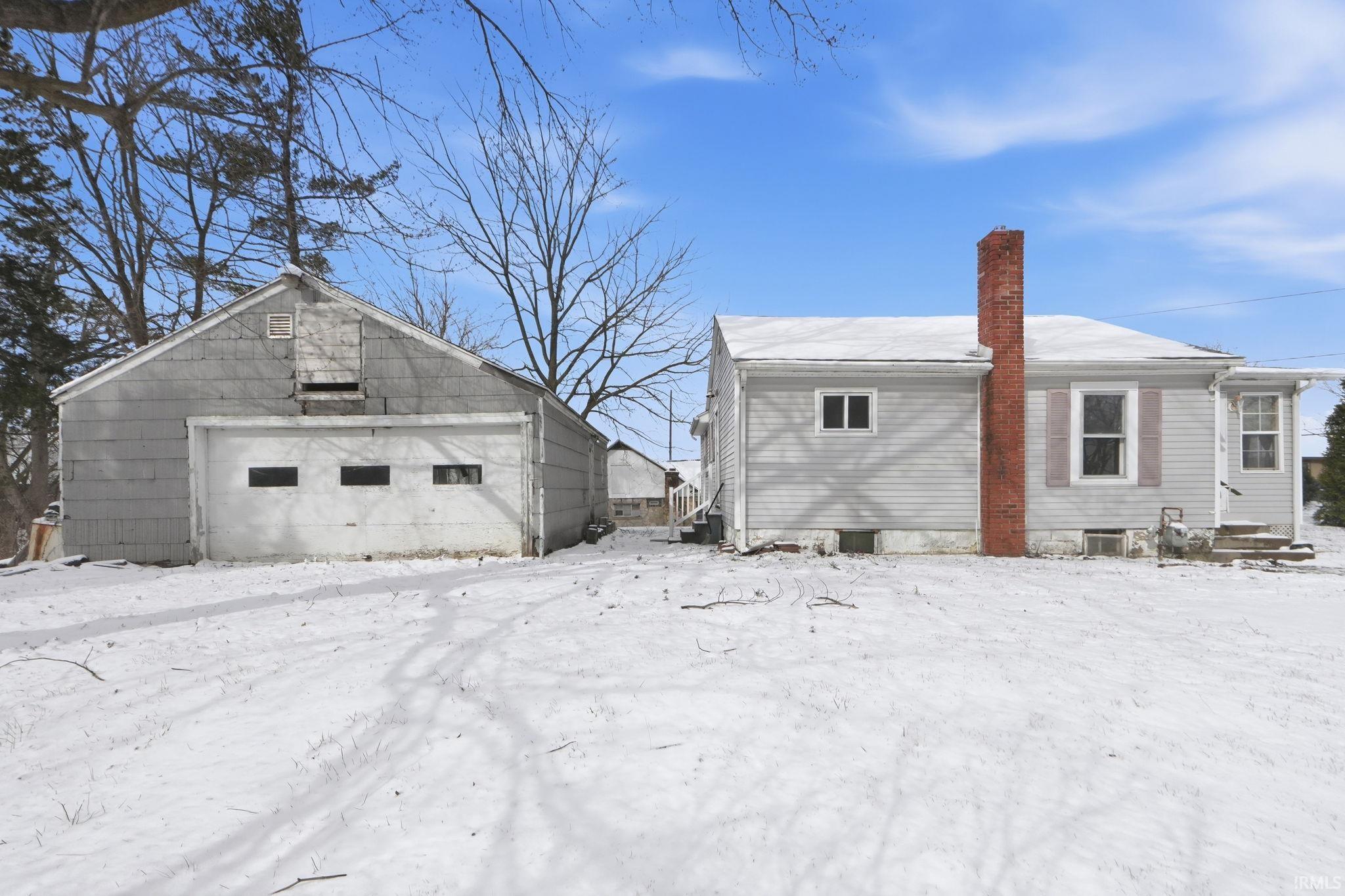 View of snowy exterior with a chimney, an outbuilding, and a garage