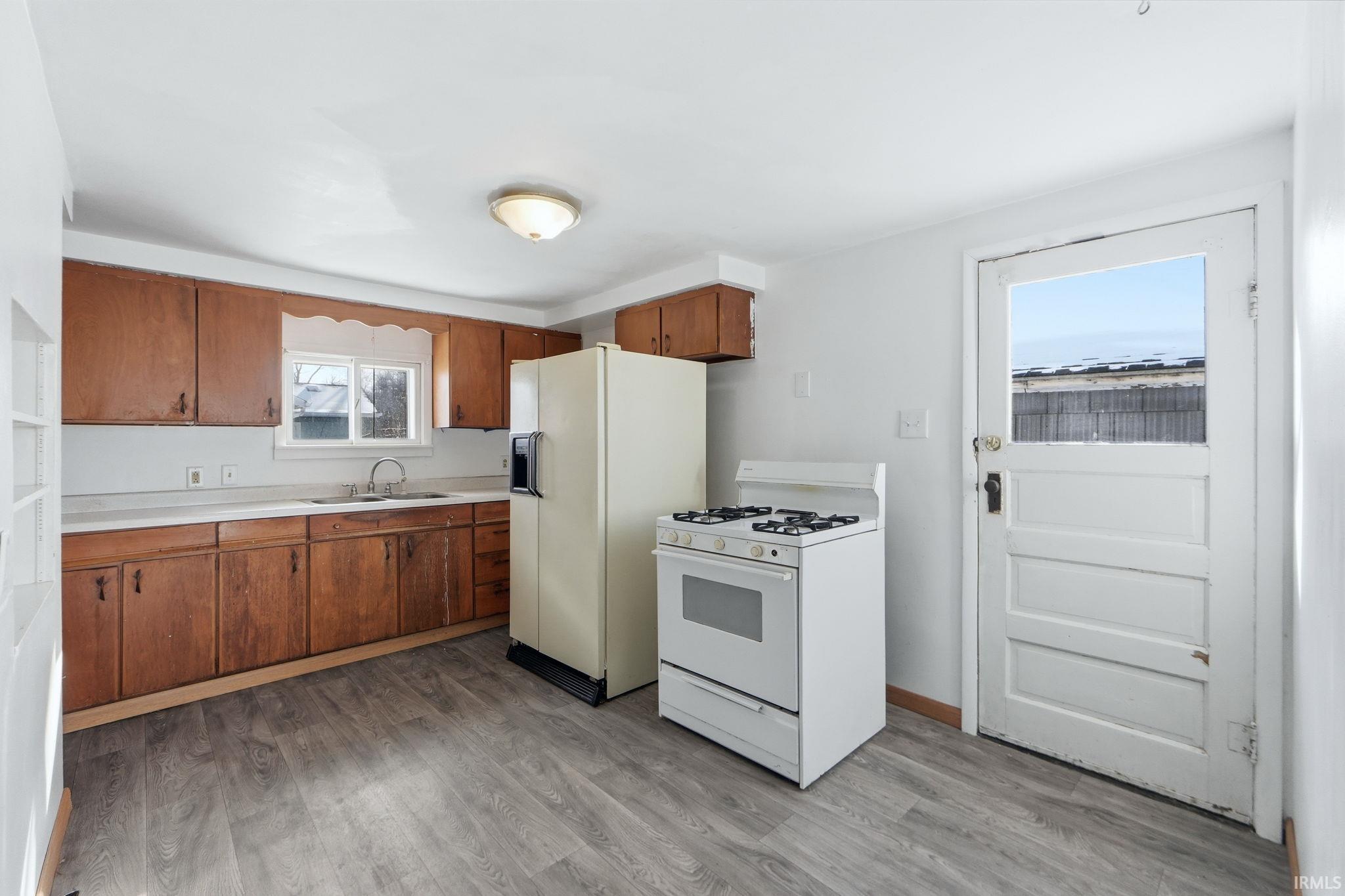 Kitchen with white appliances, wood finish cabinetry, light countertops, and light wood-style floors