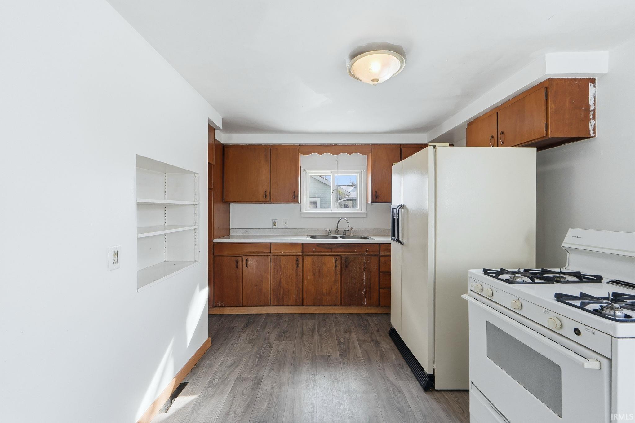 Kitchen featuring white appliances, wood finish cabinets, light countertops, and dark wood-type flooring