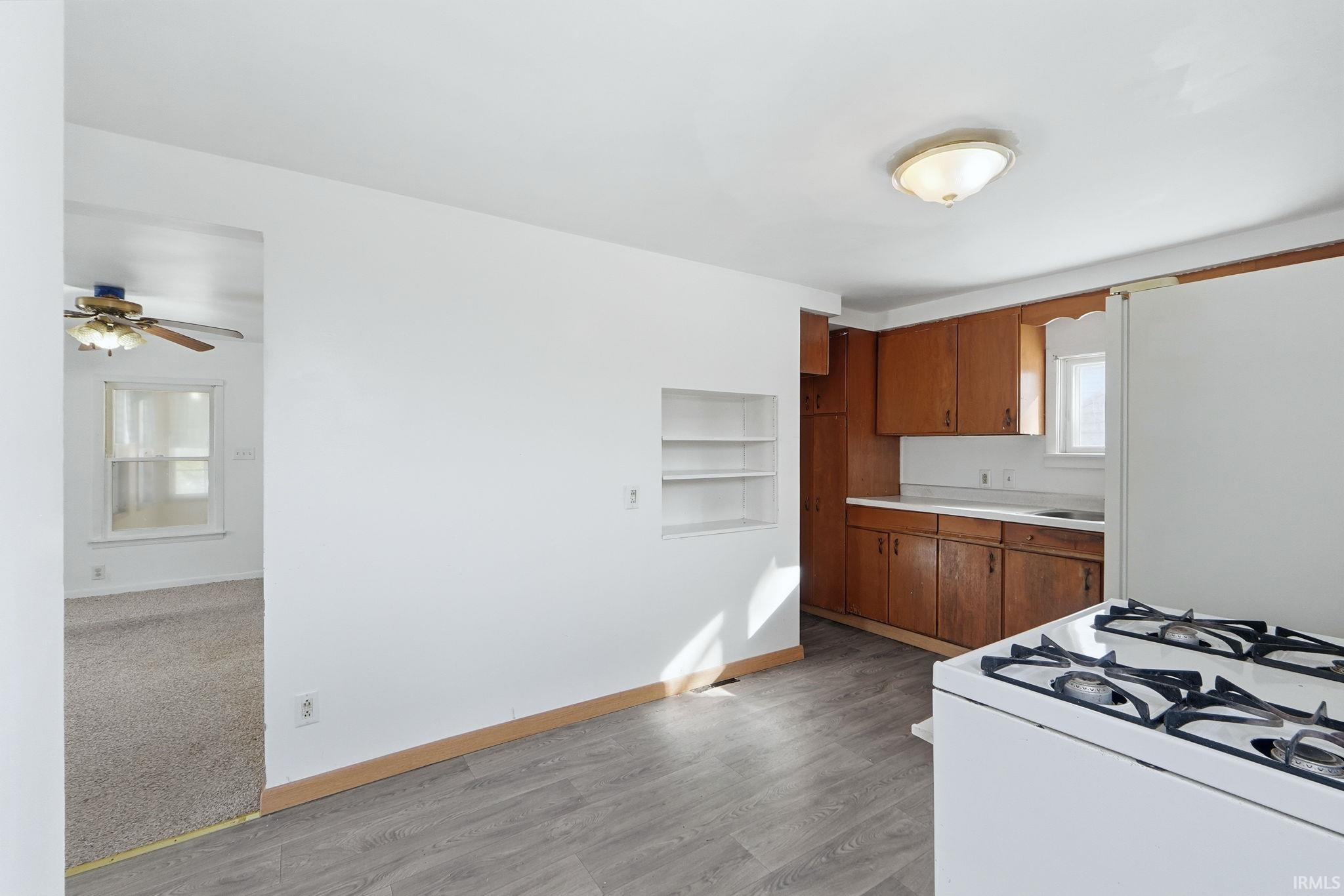 Kitchen with white appliances, wood finish cabinetry, light countertops, built in features, and light wood-style flooring