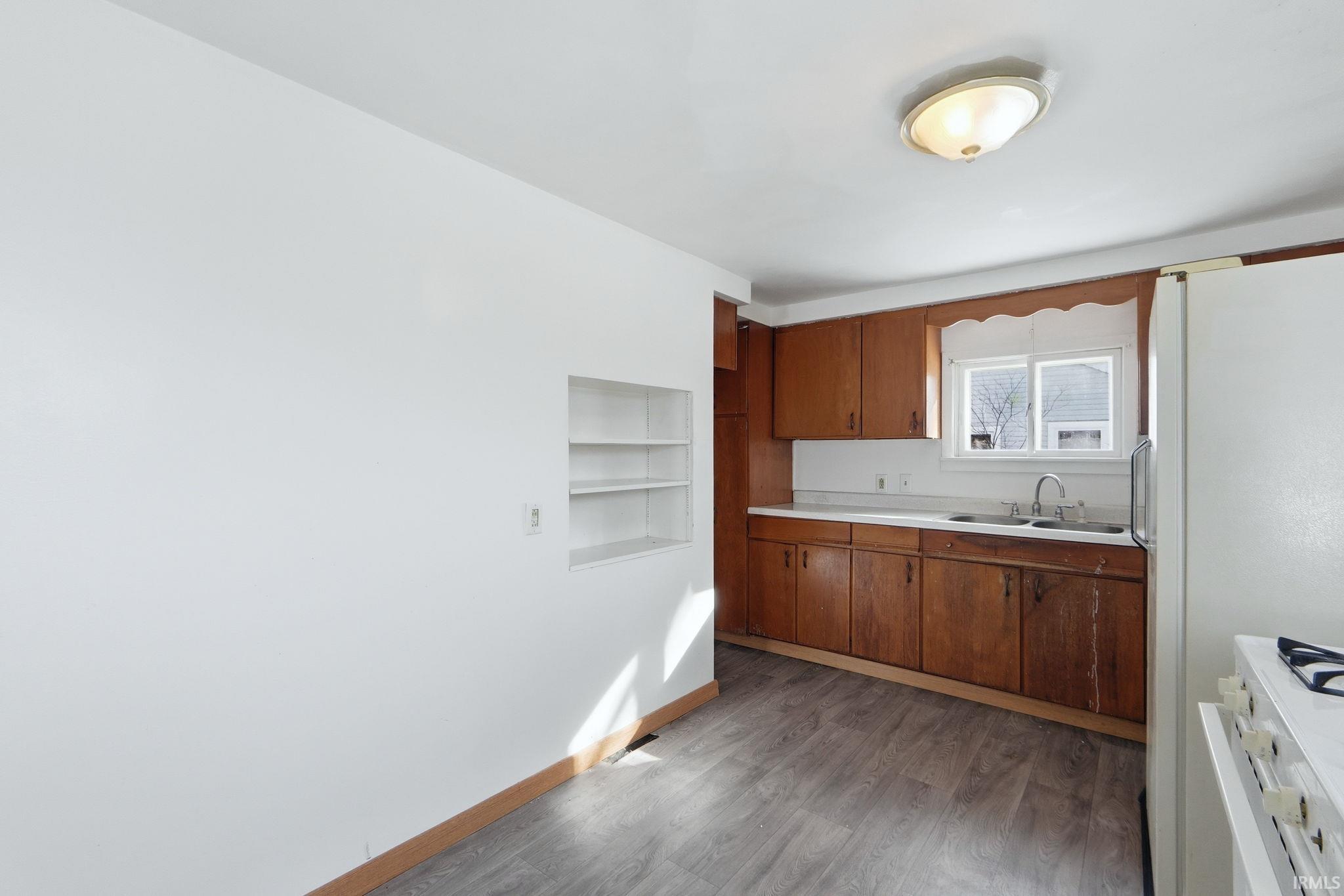 Kitchen with light countertops, wood finish cabinets, white appliances, dark wood-style floors, and built in features