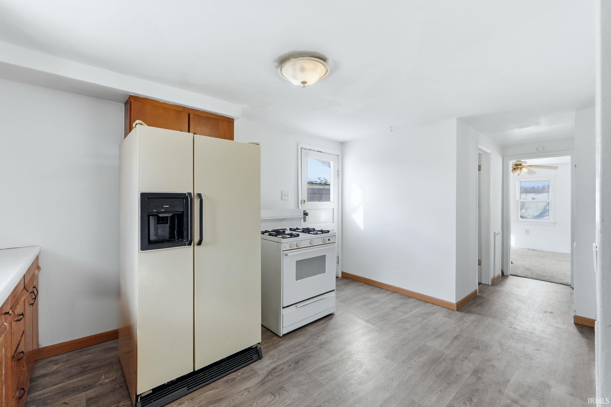 Kitchen with white appliances, wood finish cabinetry, light countertops, and light wood-style floors