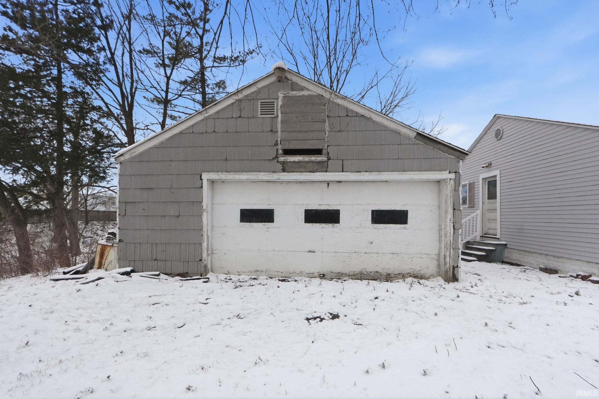 Snow covered house with an outdoor structure and a garage