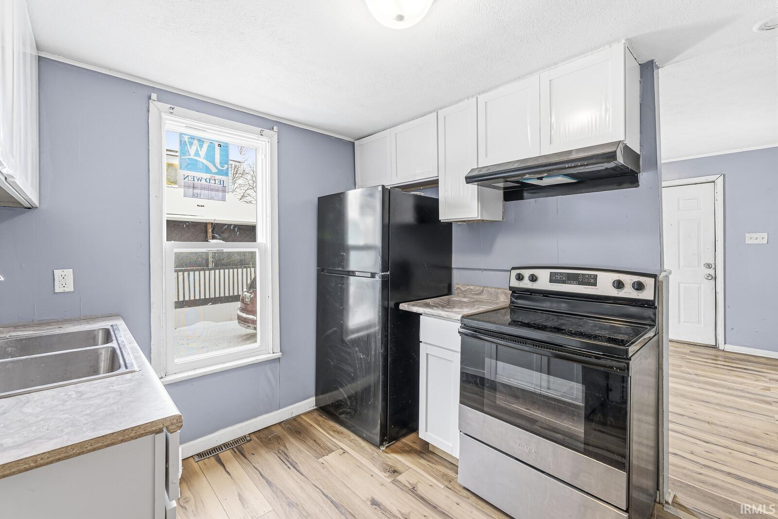 Kitchen with stainless steel range with electric cooktop, light countertops, white cabinets, freestanding refrigerator, and light wood-type flooring
