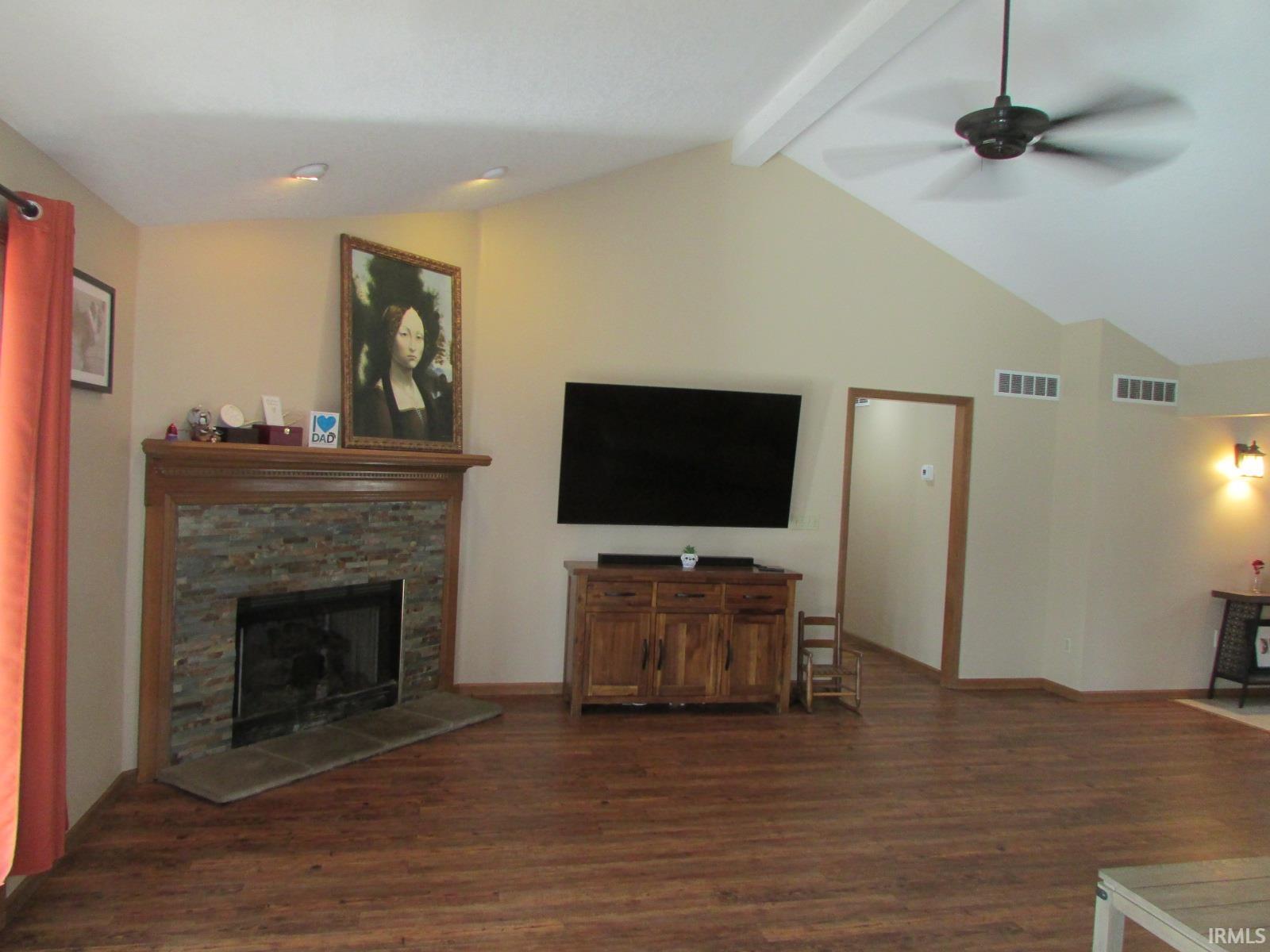 Living area with a fireplace, dark wood finished floors, beamed ceiling, and a ceiling fan