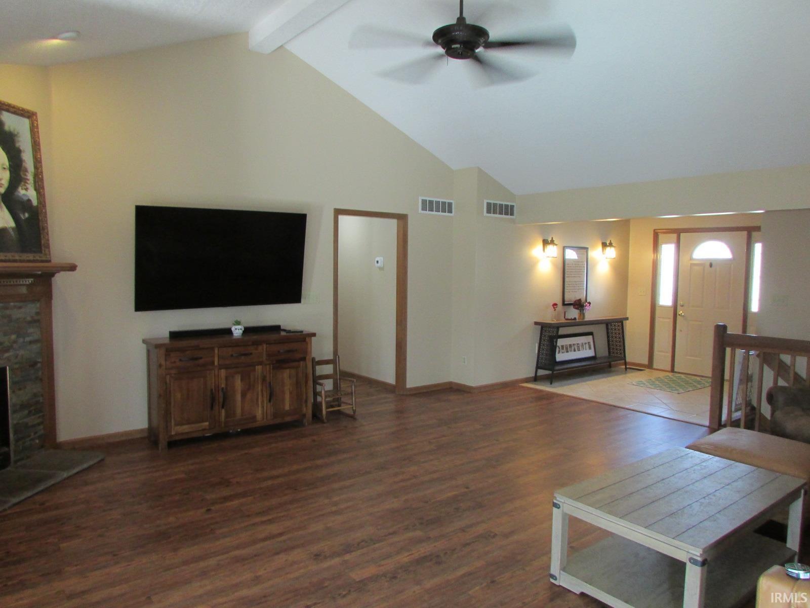 Living room with dark wood-style flooring, a ceiling fan, and a stone fireplace