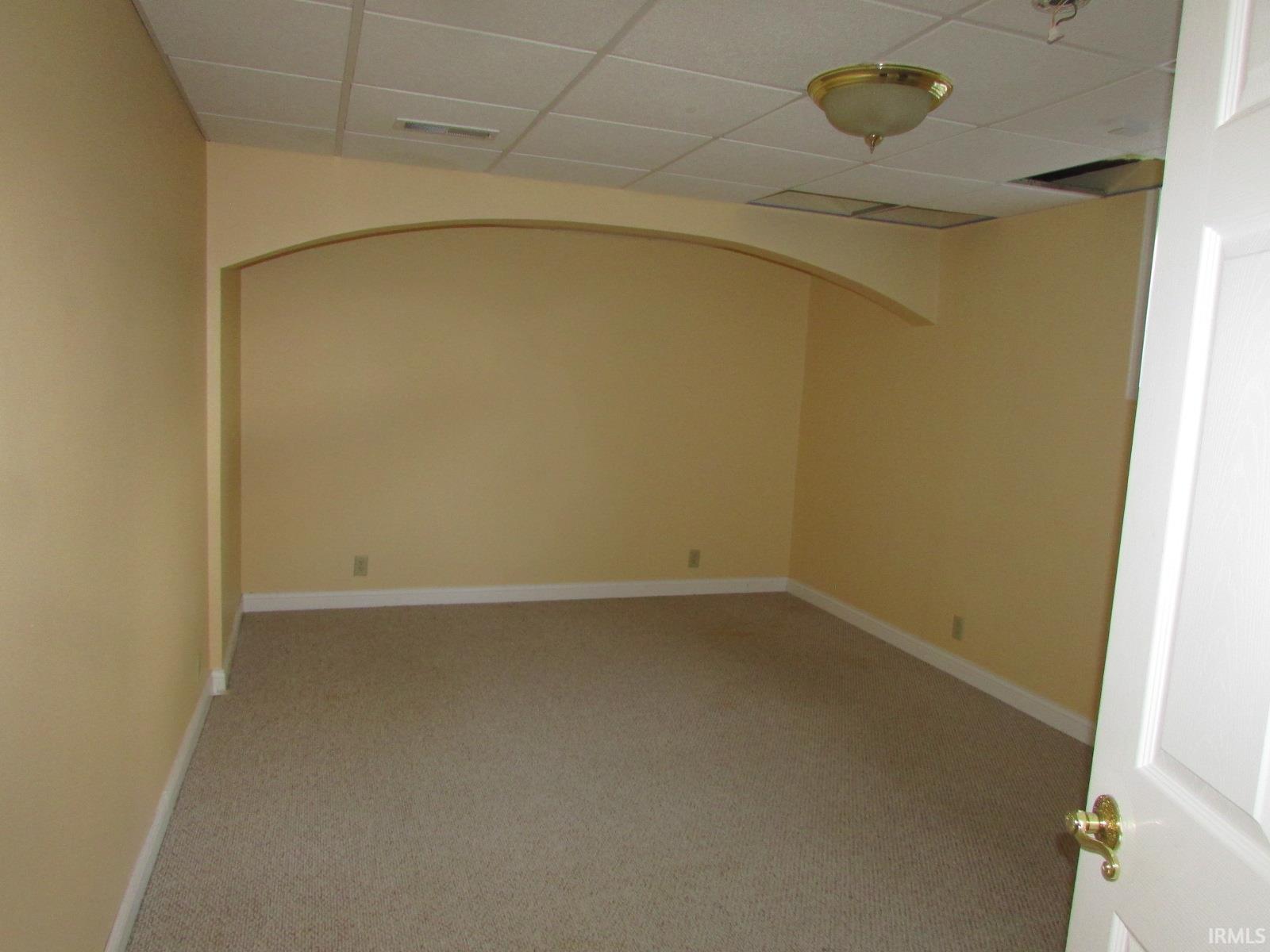 Unfurnished room featuring arched walkways, a drop ceiling, and light colored carpet