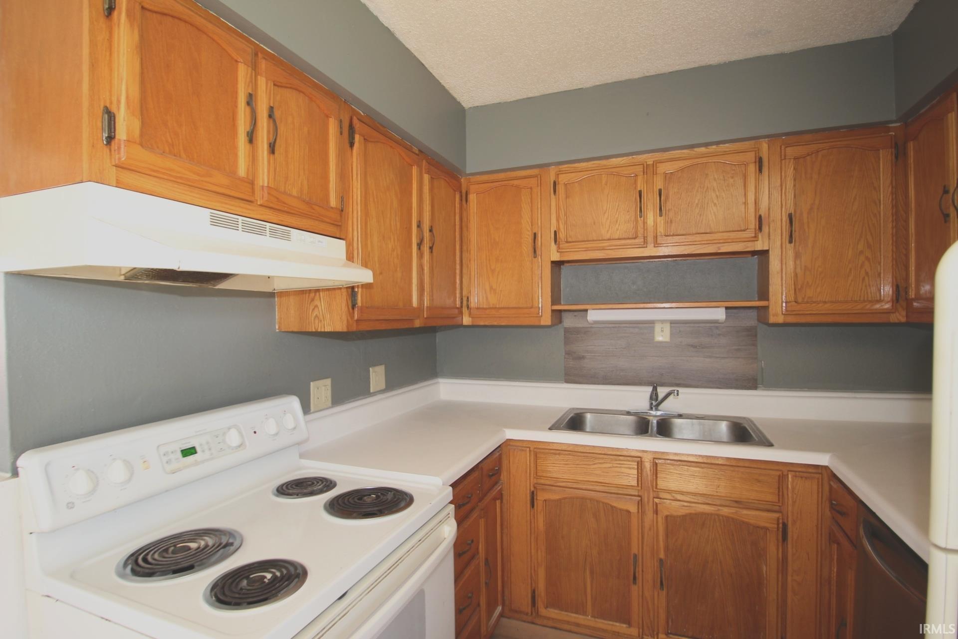 Kitchen featuring white electric range, light countertops, wood finish cabinetry, and a textured ceiling