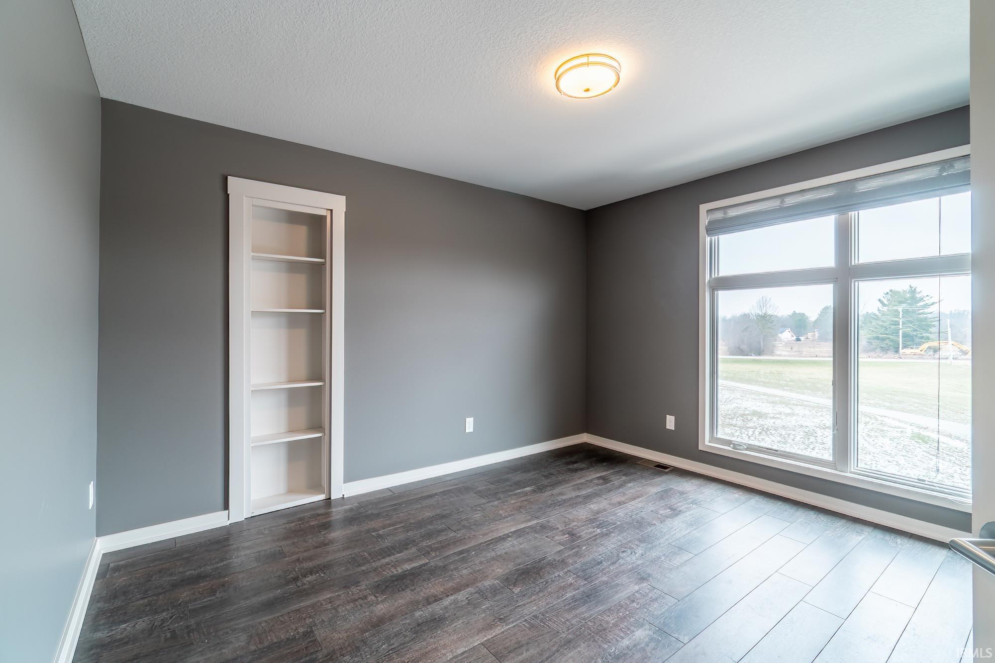 Unfurnished room with built in shelves and dark wood-type flooring