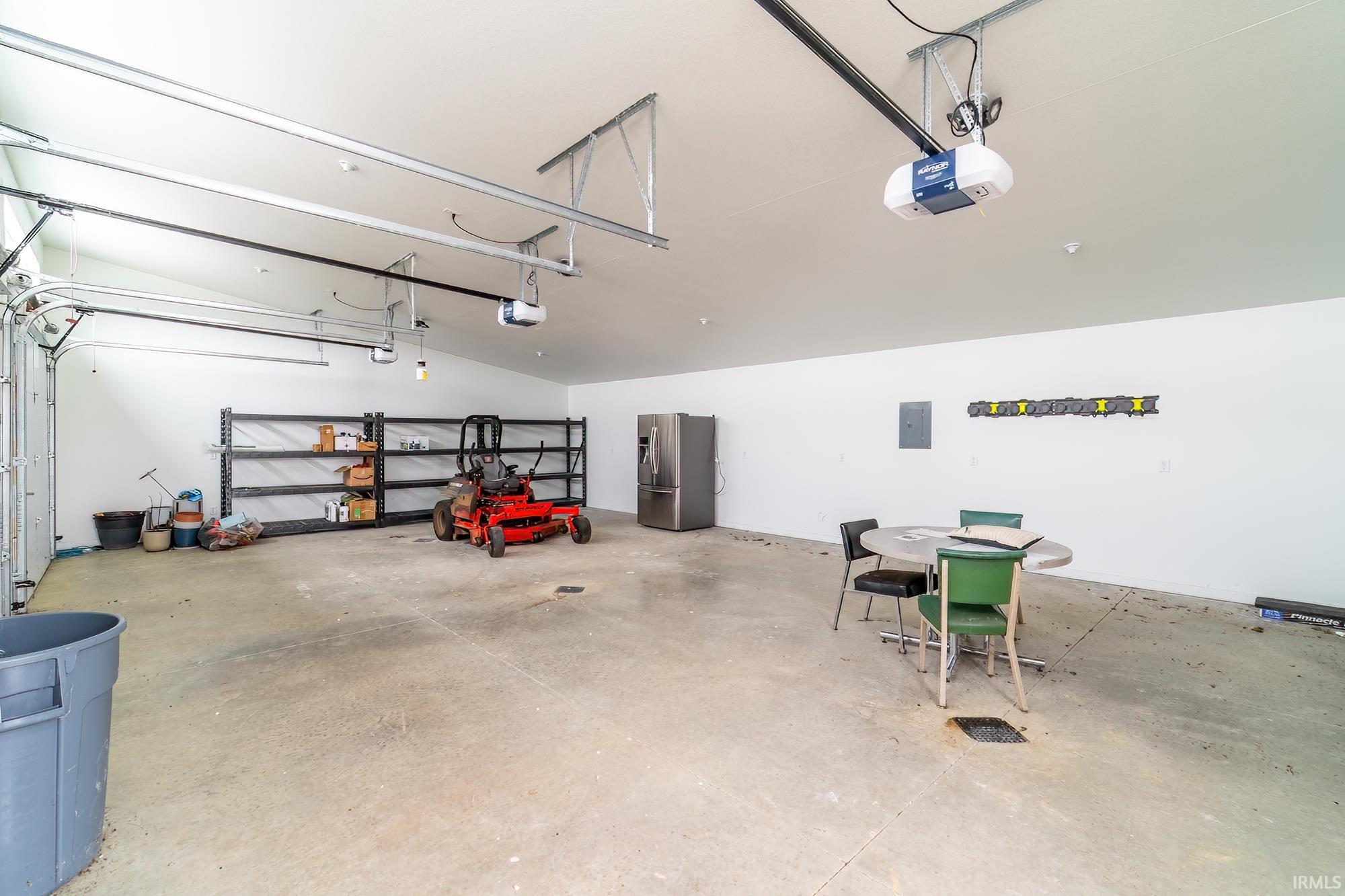 Garage featuring stainless steel refrigerator with ice dispenser, electric panel, and a garage door opener