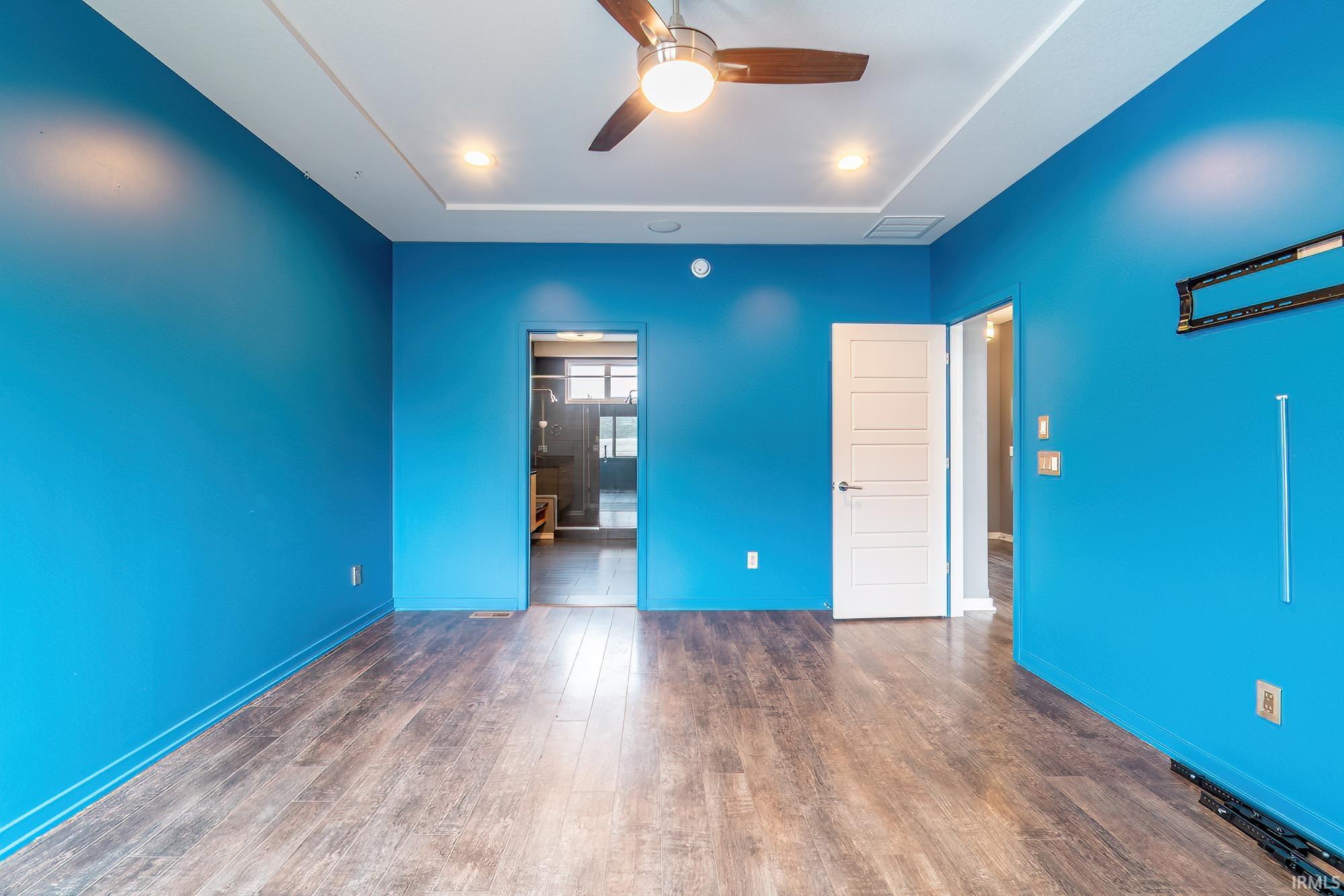 Unfurnished bedroom featuring dark wood finished floors, a ceiling fan, connected bathroom, and a tray ceiling