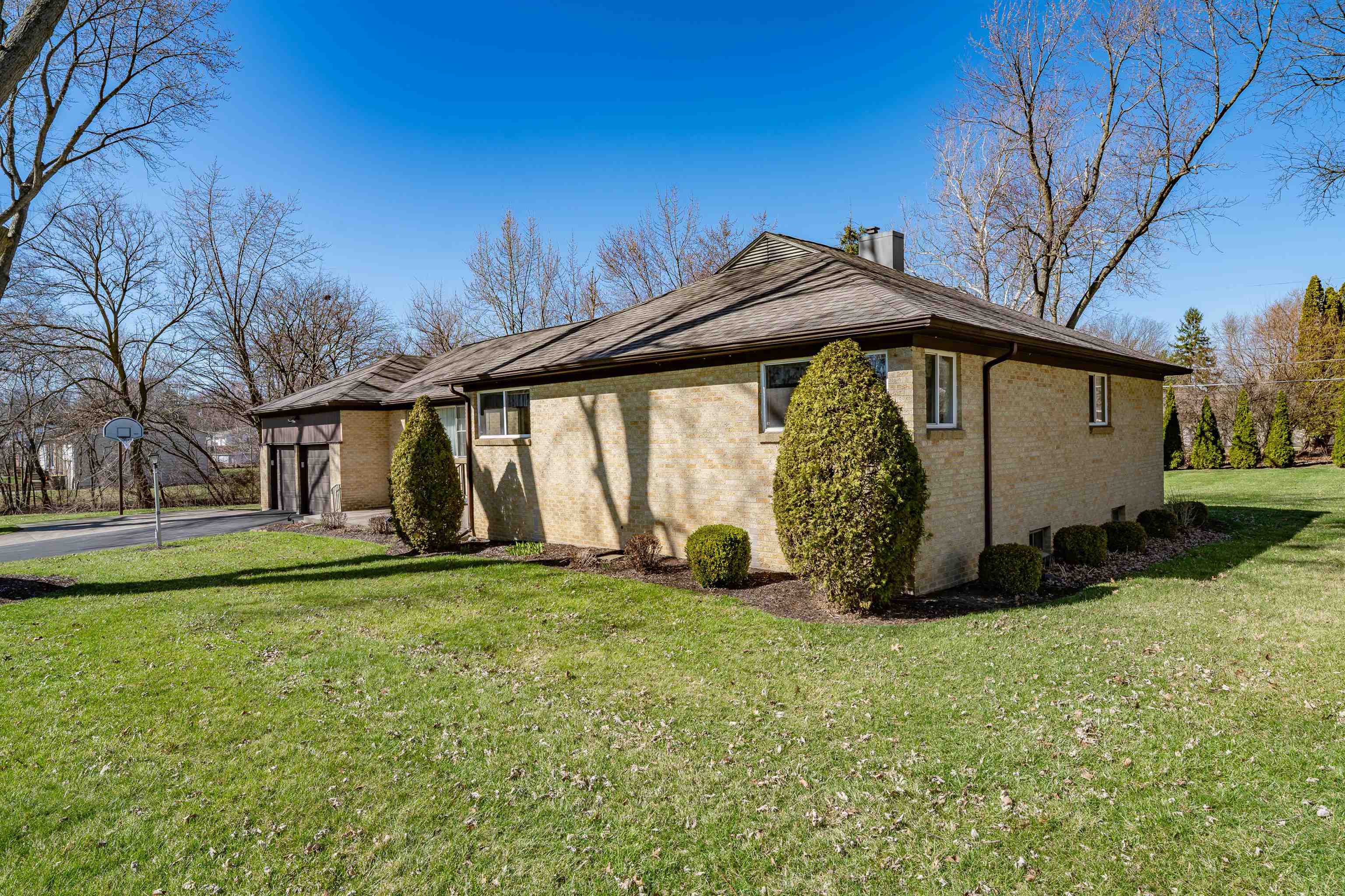 View of home's exterior with brick siding, a lawn, a garage, asphalt driveway, and a chimney