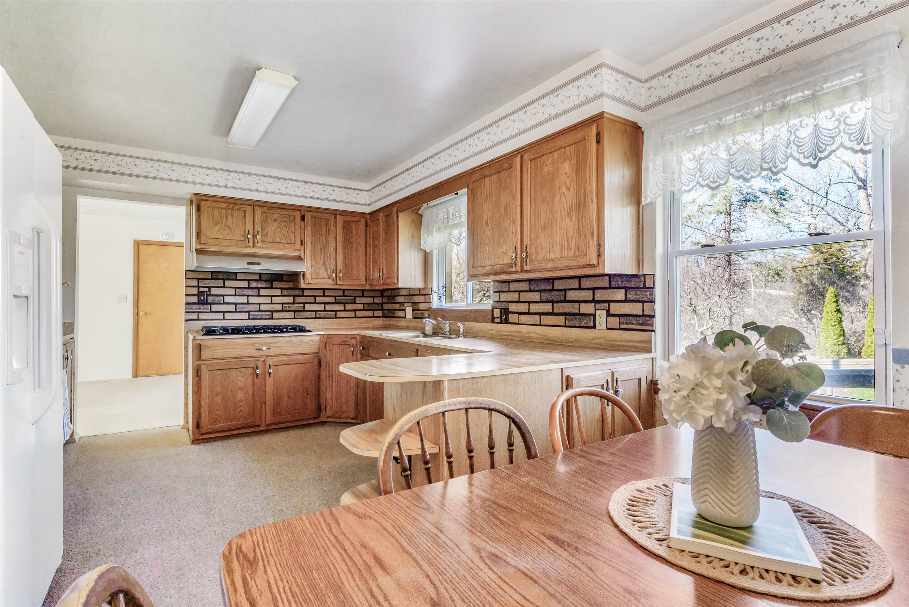 Kitchen featuring light countertops, a peninsula, white fridge with ice dispenser, tasteful backsplash, and wood finish cabinetry