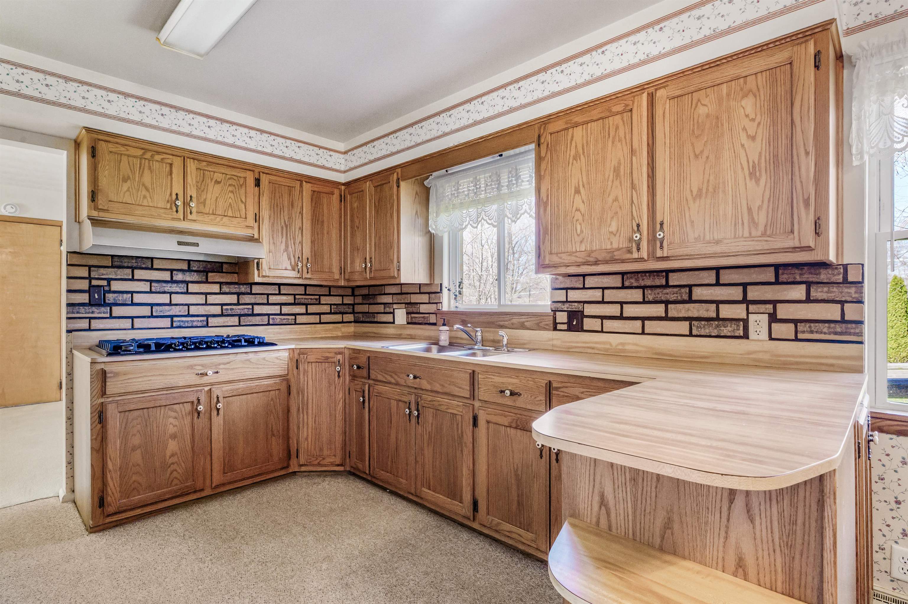 Kitchen featuring light countertops, a peninsula, wood finish cabinetry, black gas cooktop, and tasteful backsplash
