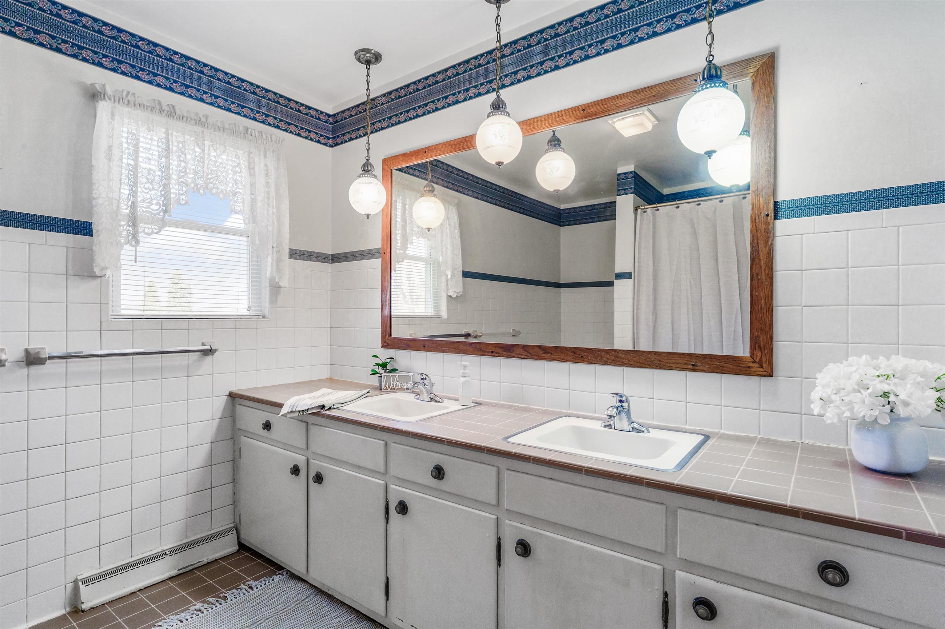 Bathroom with double vanity, a baseboard radiator, tile walls, a wainscoted wall, and a shower with curtain