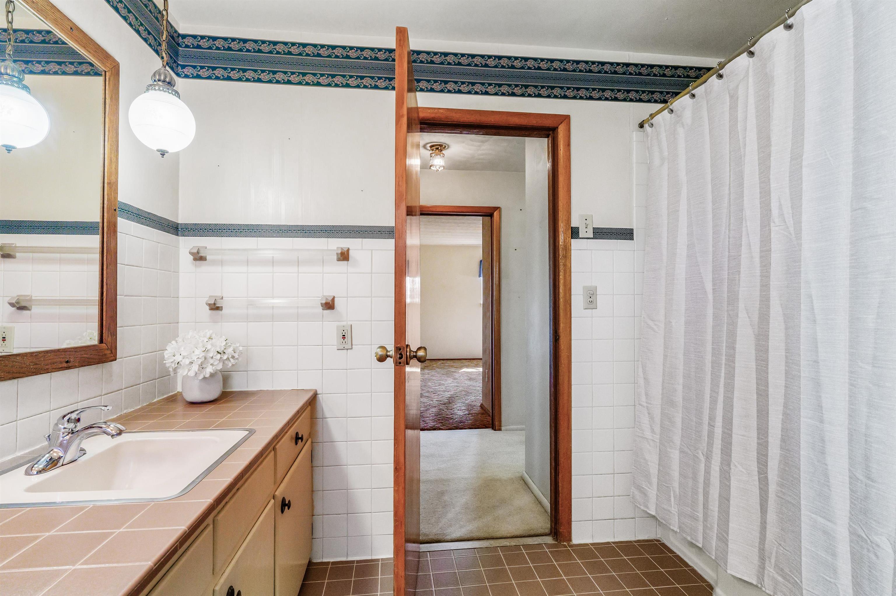 Full bath with vanity, a shower with shower curtain, tile walls, and wainscoting