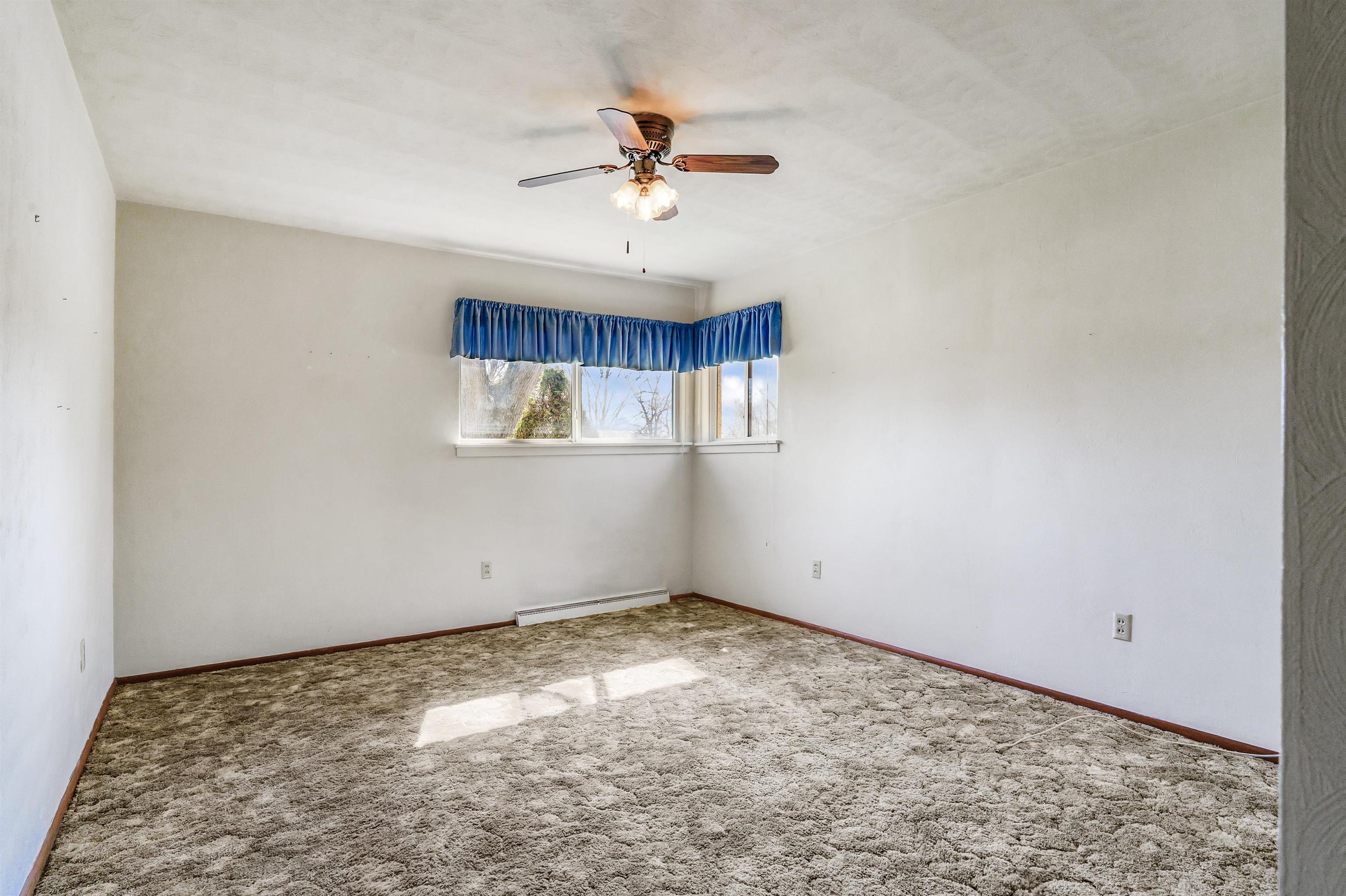 Carpeted spare room featuring ceiling fan and a baseboard radiator