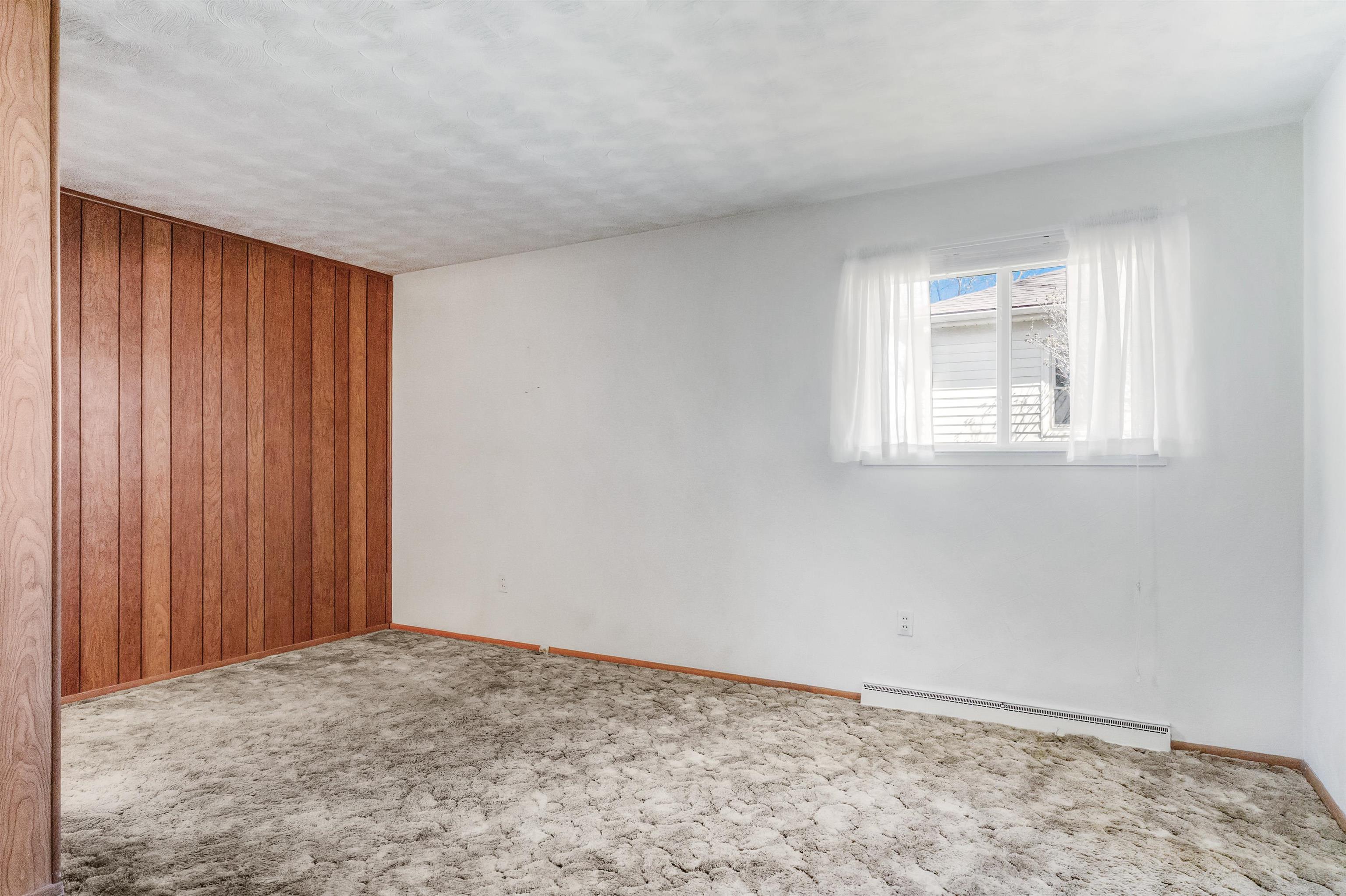 Spare room featuring wood walls, carpet, a baseboard heating unit, and a textured ceiling