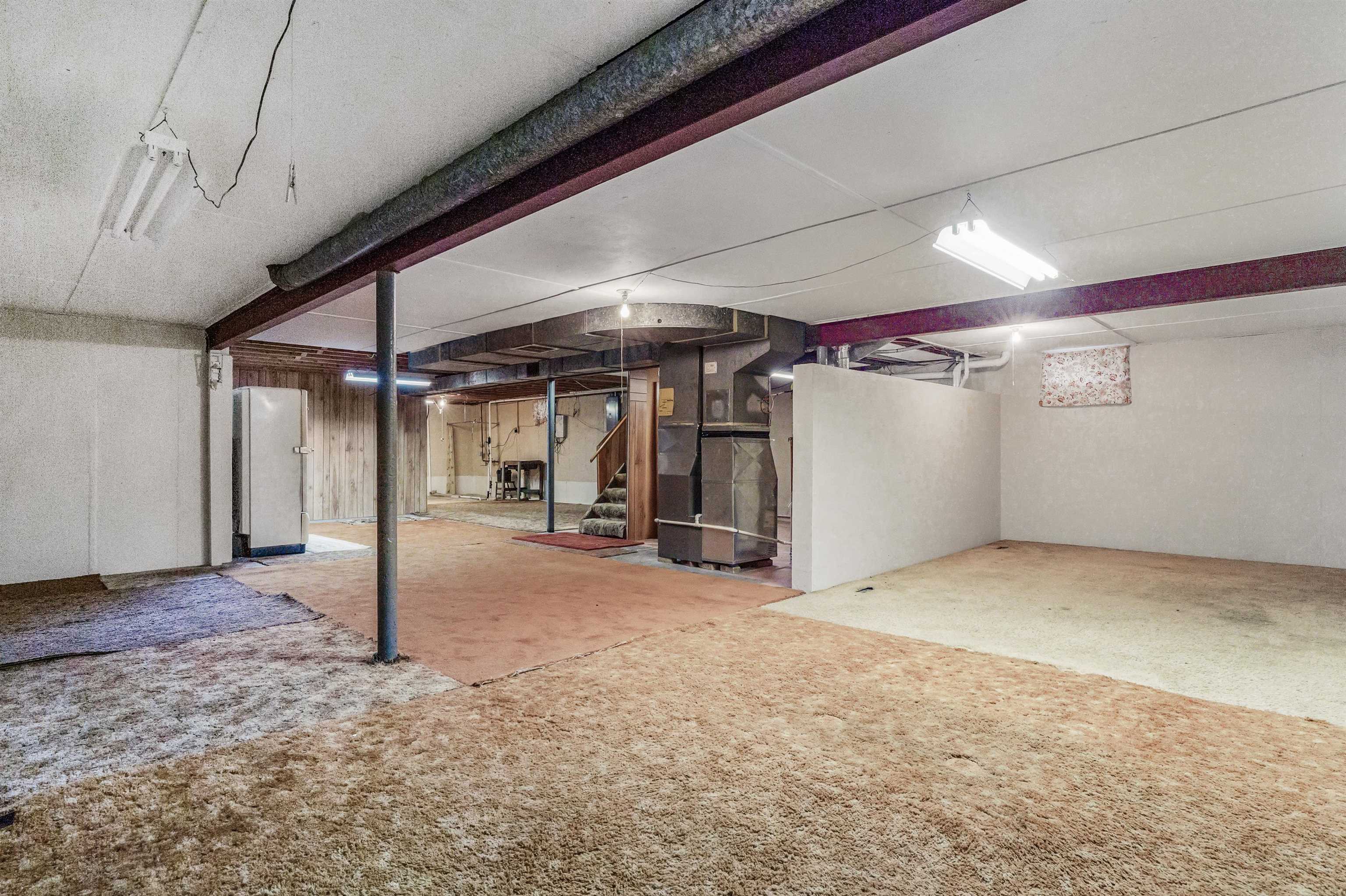 Unfinished below grade area featuring heating unit, carpet flooring, and freestanding refrigerator