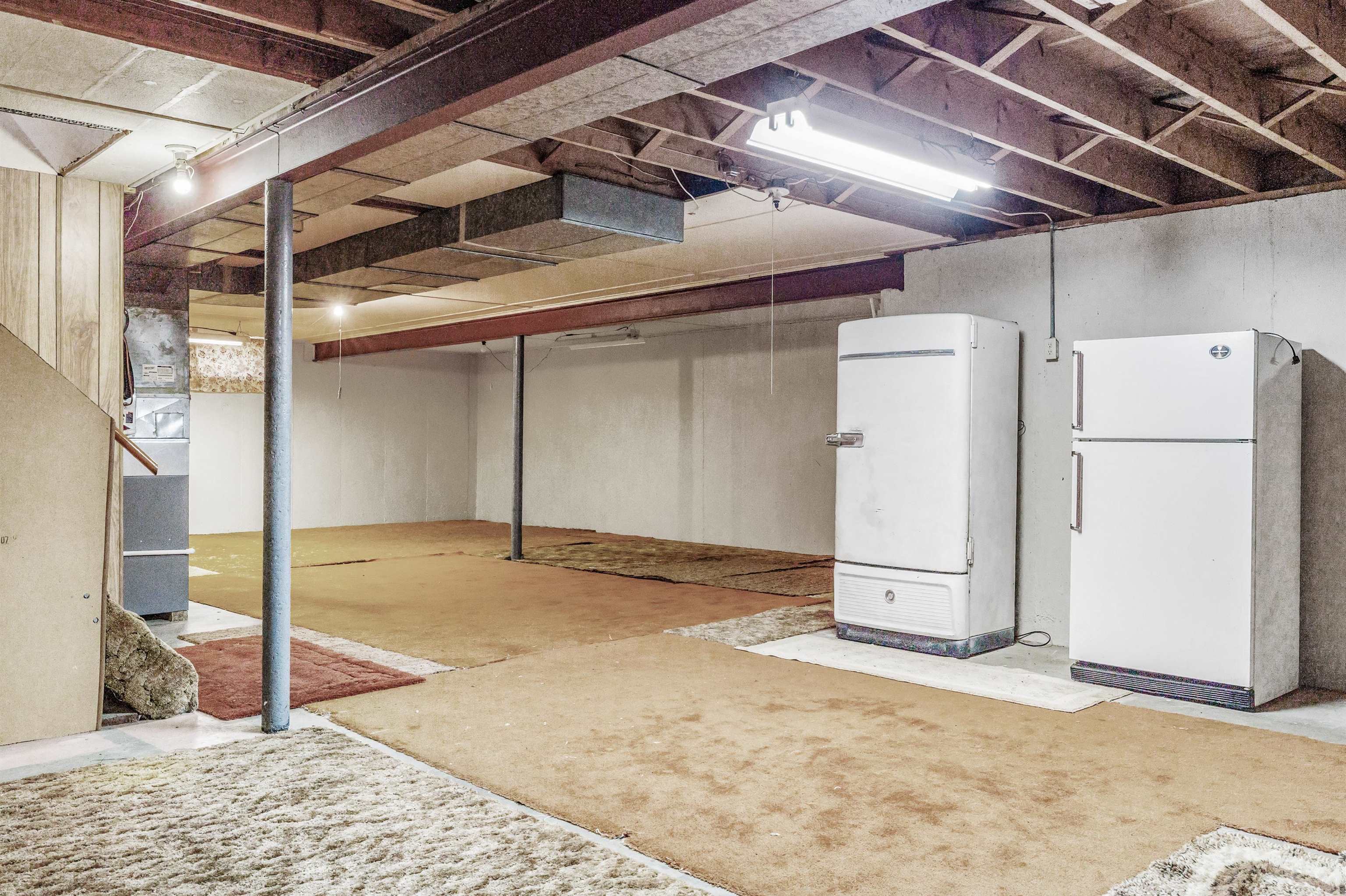 Unfinished below grade area with freestanding refrigerator and heating unit