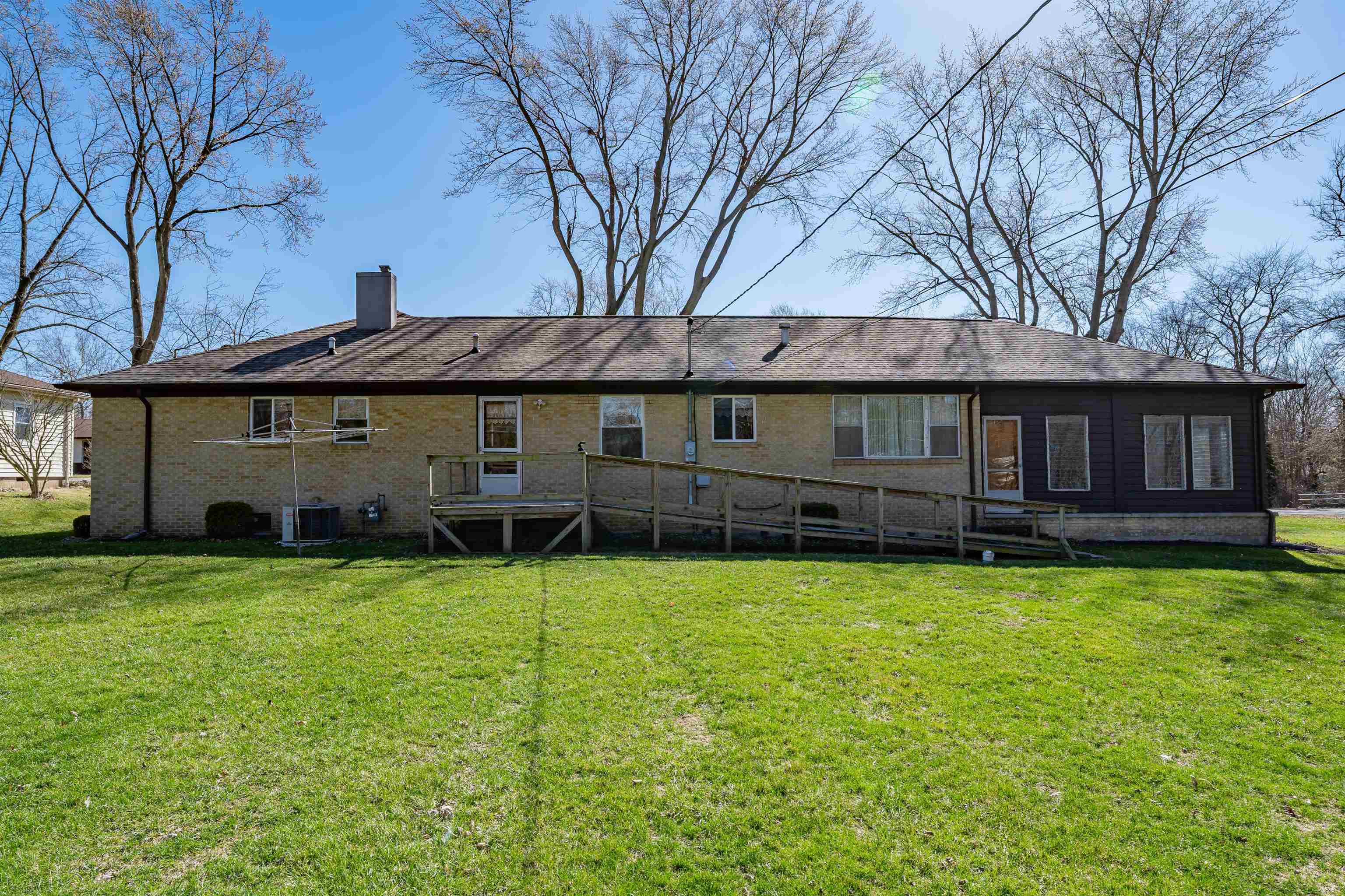 Back of house featuring a yard, a chimney, brick siding, and a deck