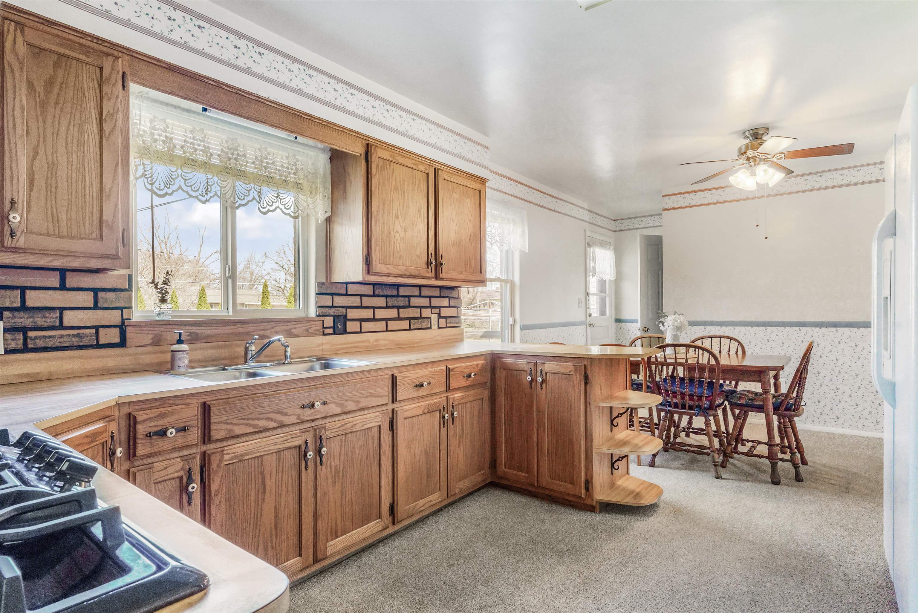 Kitchen featuring wallpapered walls, wood finish cabinetry, a peninsula, light countertops, and a ceiling fan