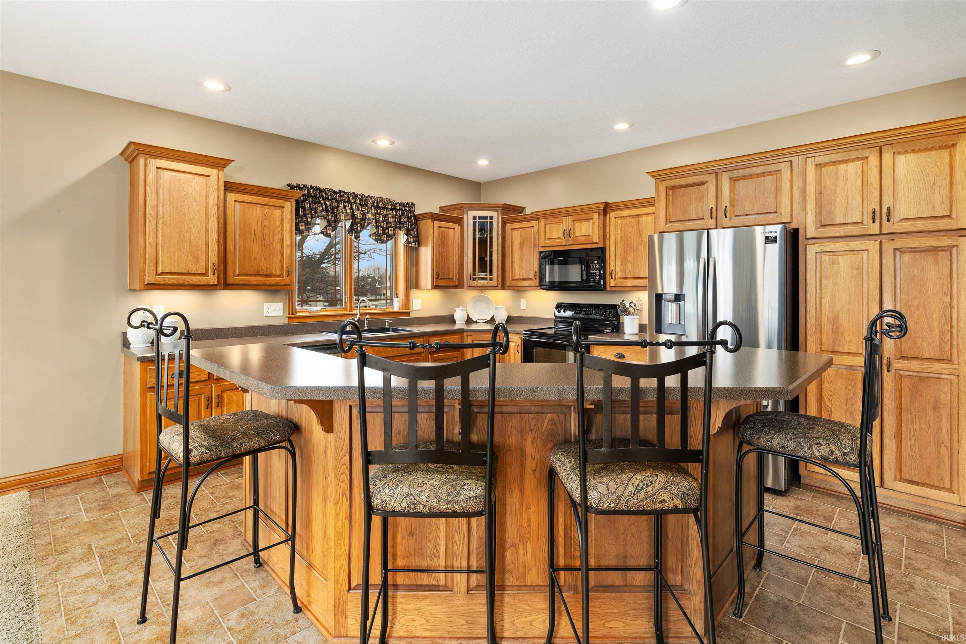Kitchen featuring dark countertops, a center island with sink, a kitchen bar, wood finish cabinets, and black appliances