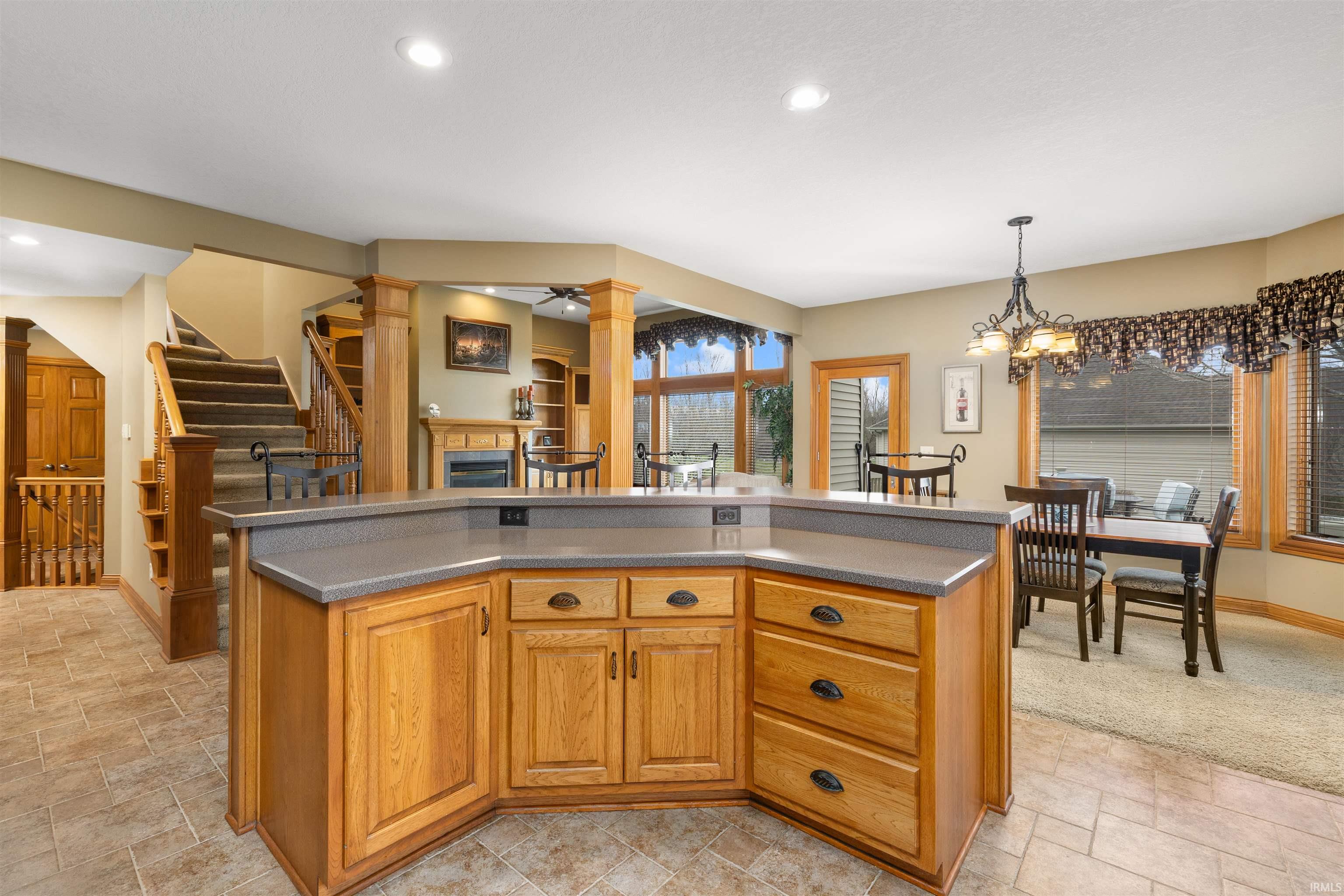 Kitchen featuring ornate columns, a center island, light stone finish flooring, a chandelier, and a tiled fireplace